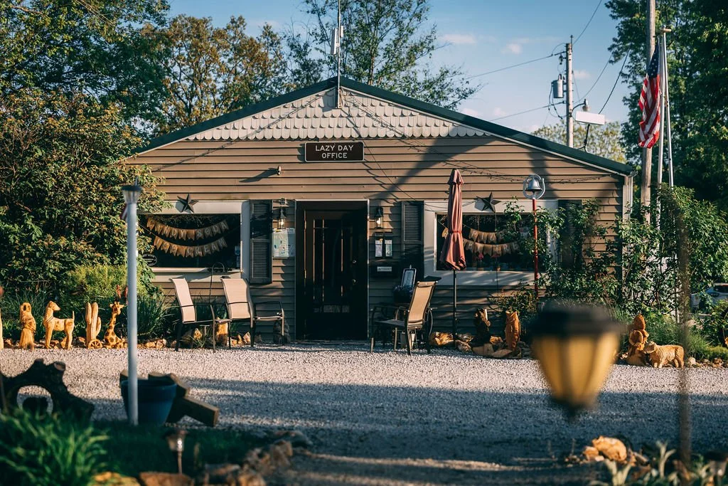 A small building labeled 'Lazy Day Office' with outdoor seating, decorative plants, and animal figurines in front.