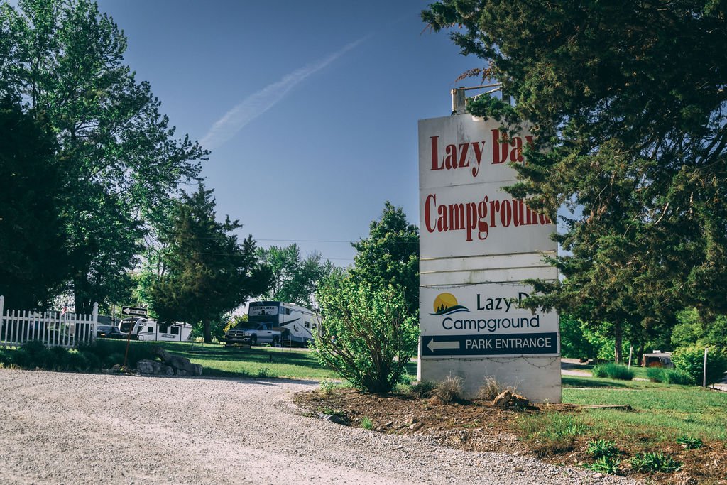Sign for Lazy Day Campground with directions, surrounded by trees and a gravel driveway.