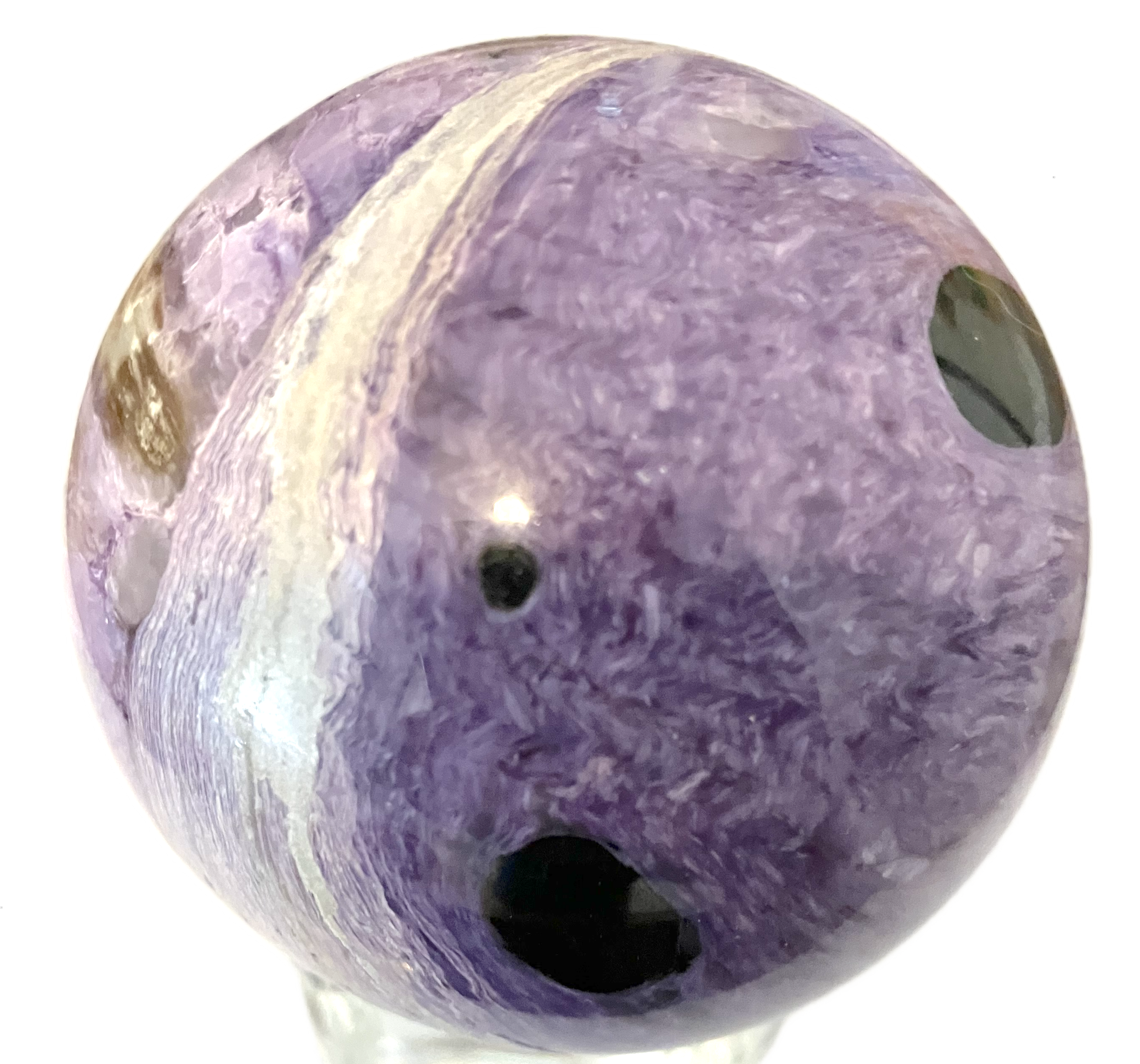 Close-up of a polished purple crystal stone with darker spots and striations.