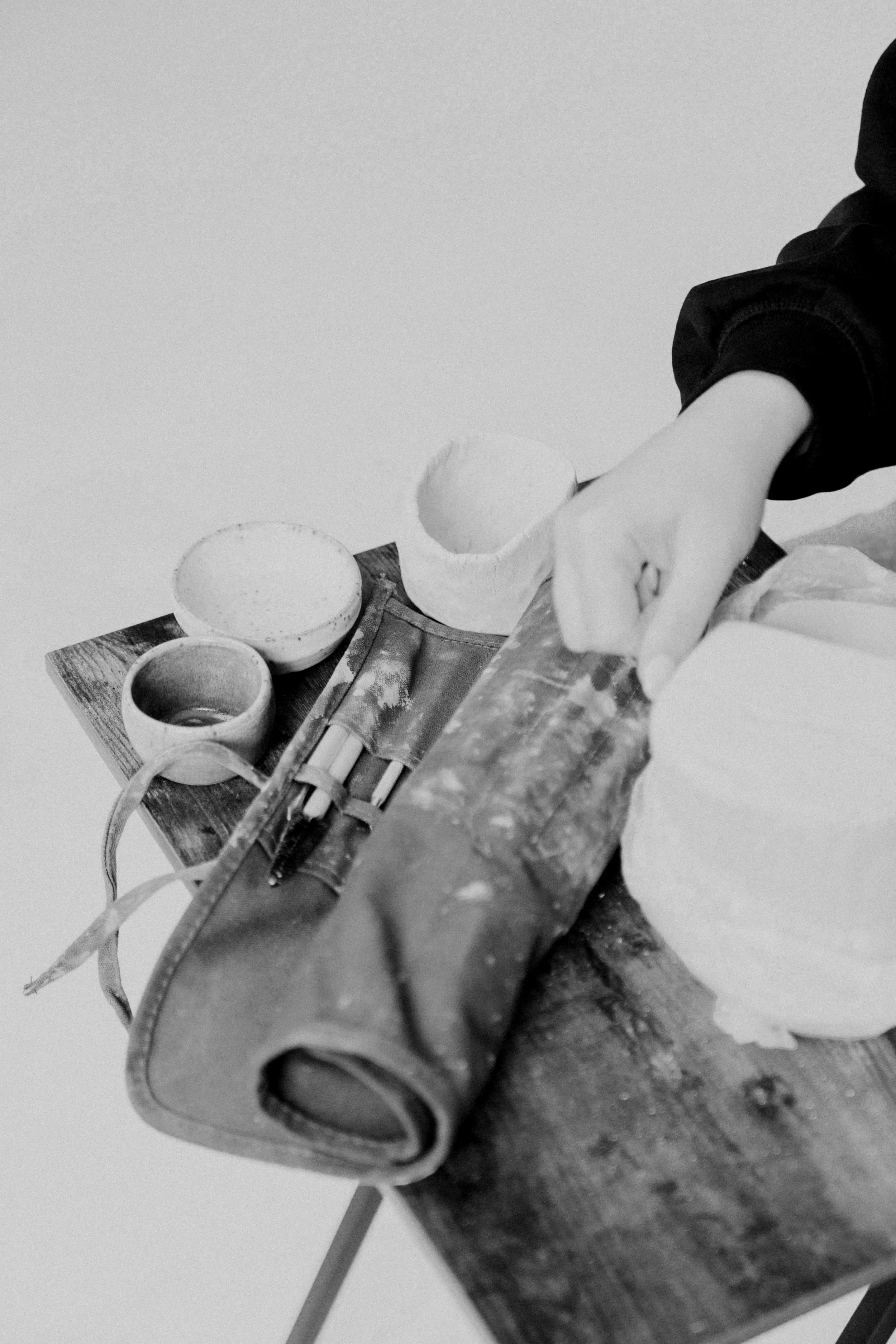 Black and white photo of a person's arm holding a binary digit, with pottery cups and a wooden slice displayed on a table.