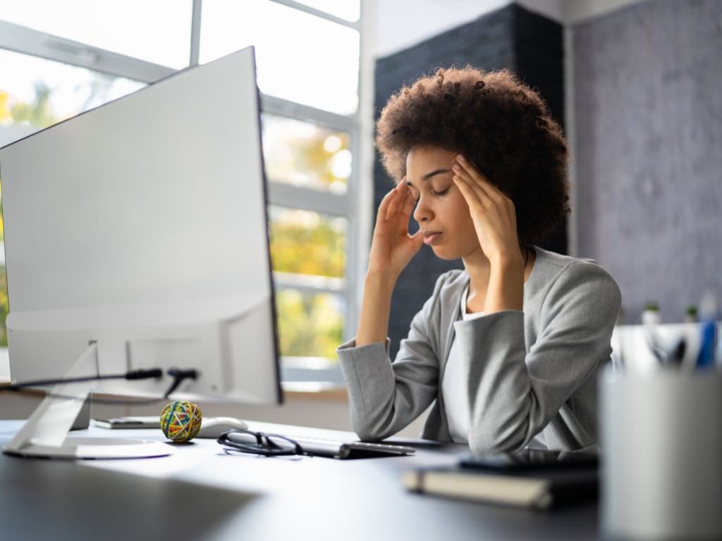 A high-achieving woman sitting at her desk feeling overwhelmed by stress, perfectionism, and emotional exhaustion