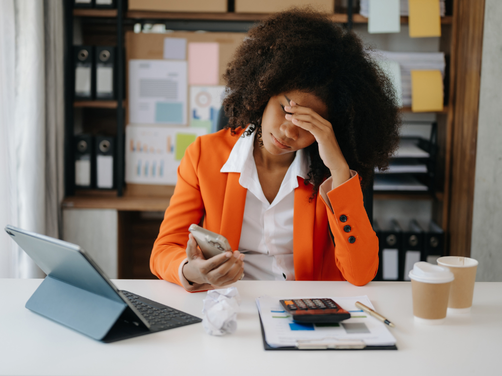 Professional Black woman working at a desk appearing overwhelmed and emotionally exhausted.