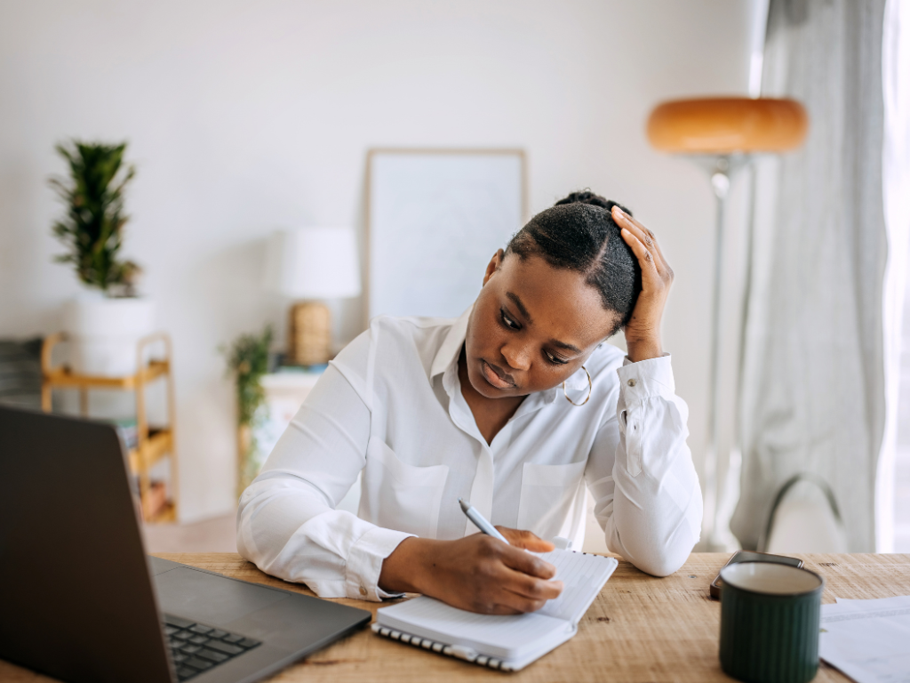 Exhausted professional woman resting her head on her hands while working on a laptop.