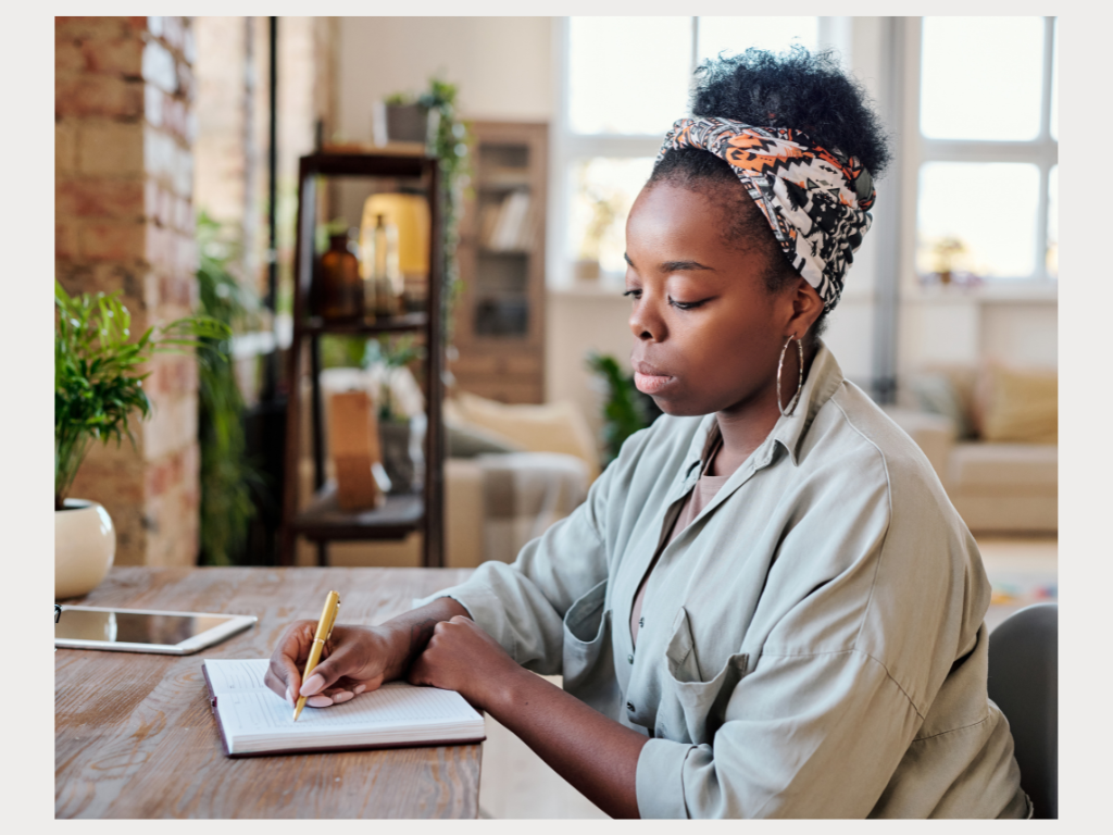 A woman writing in a journal at a tidy desk, using writing as a grounding tool for anxiety and overthinking