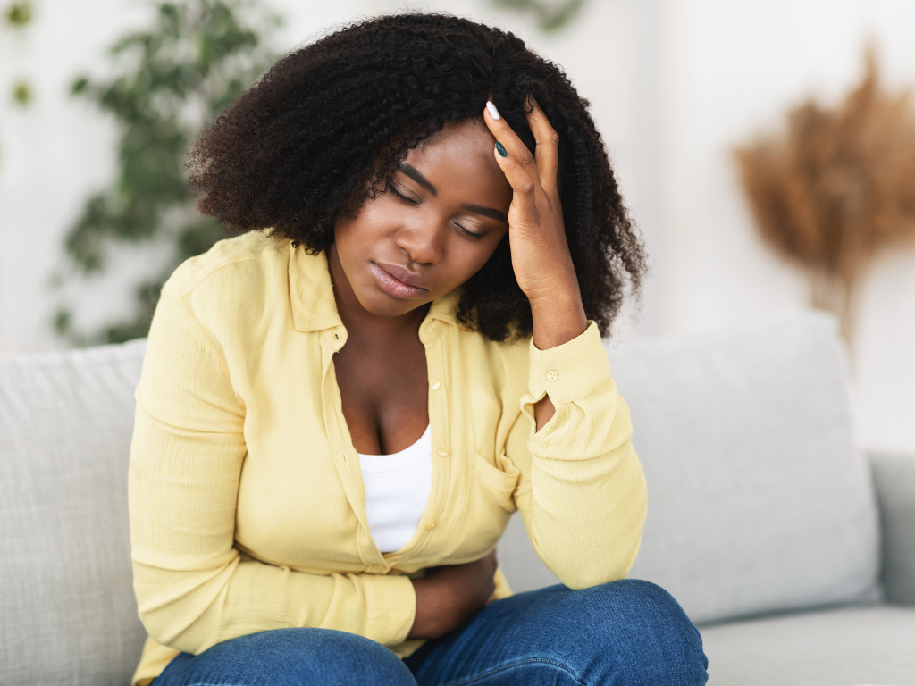 Black woman sitting alone looking tired while carrying emotional and mental burdens associated with chronic stress.