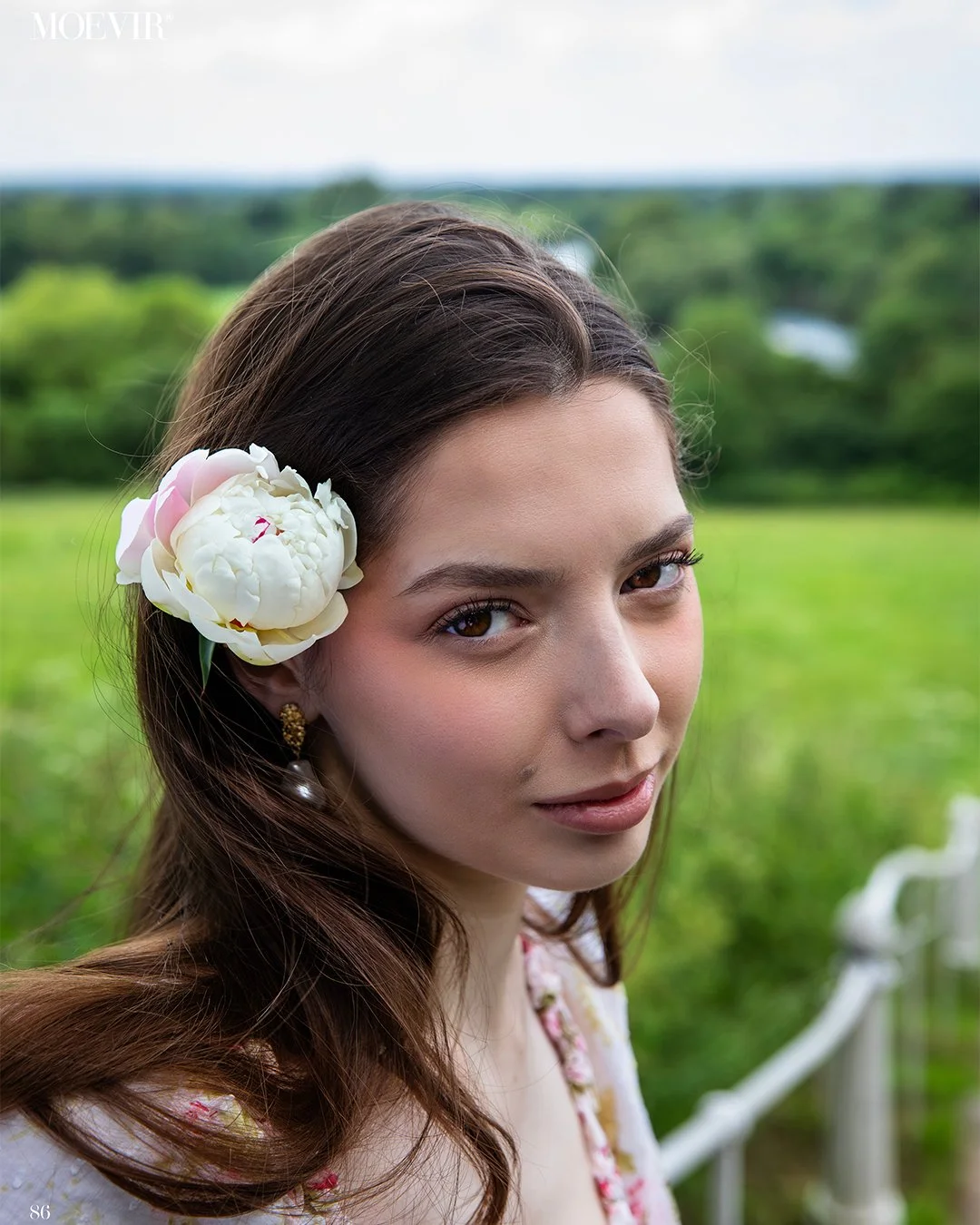 Young woman with beautiful natural makeup in a white floral dress in a magazine cover. Flower behind her ear