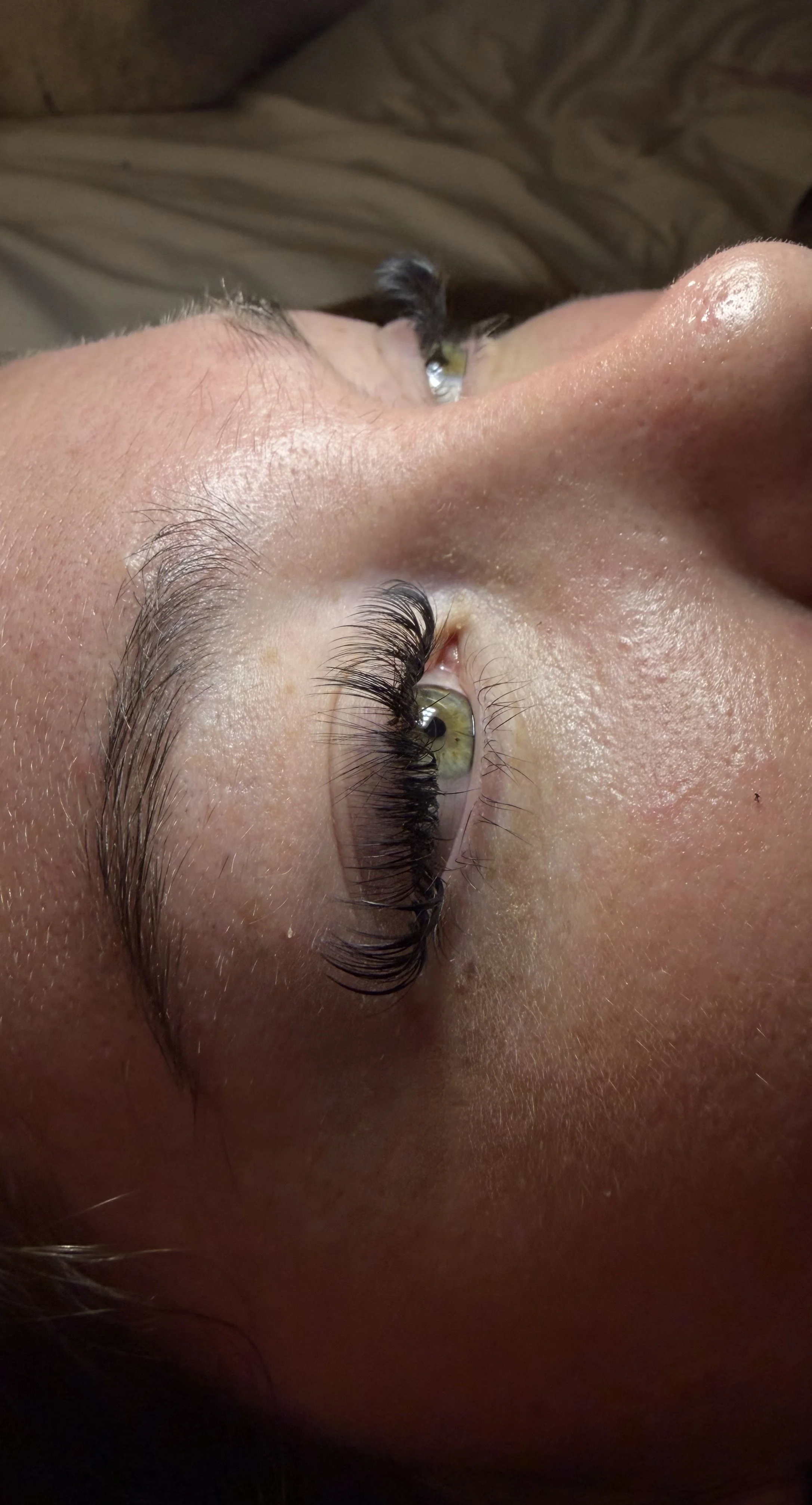 Close-up of a person's face lying down, showing their eye with long eyelashes, and a portion of their nose and forehead.