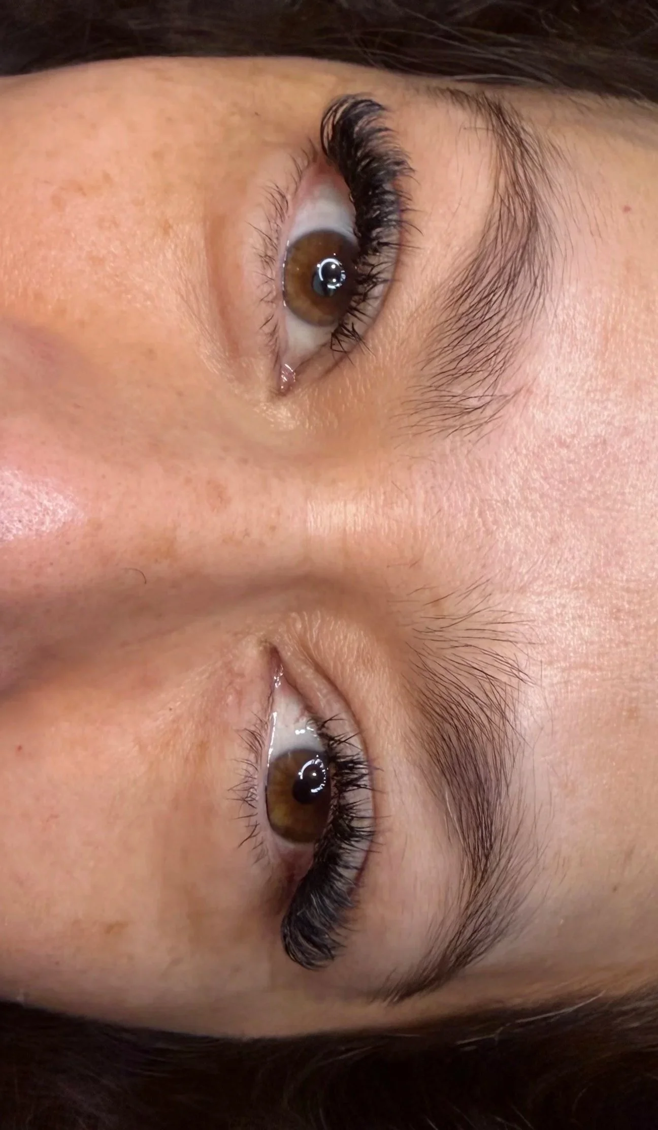 Close-up of a person's face with focus on brown eyes, emphasizing long eyelashes and eyebrows, and clear skin.