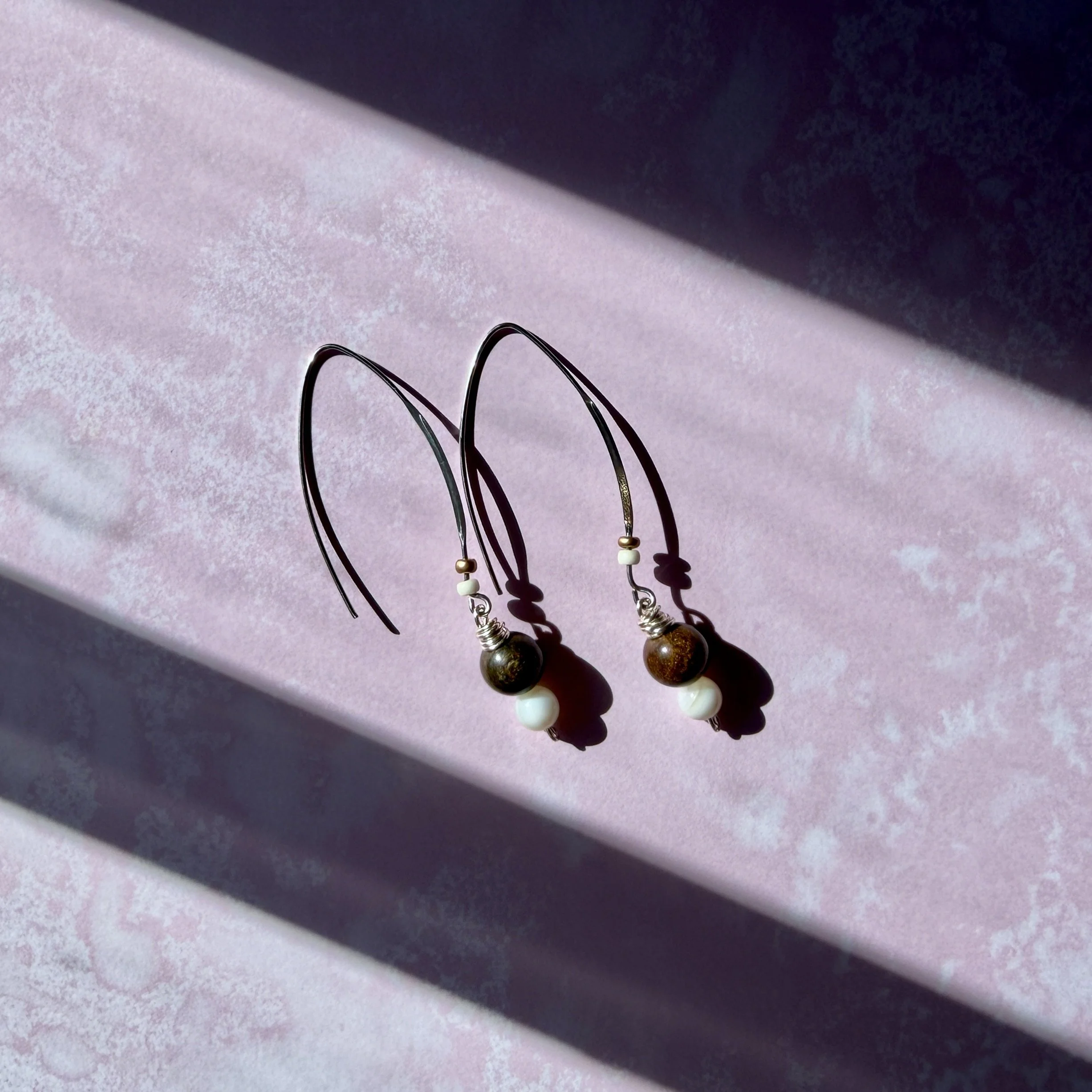 Bronzite and mother of pearl drop earrings on a pink background