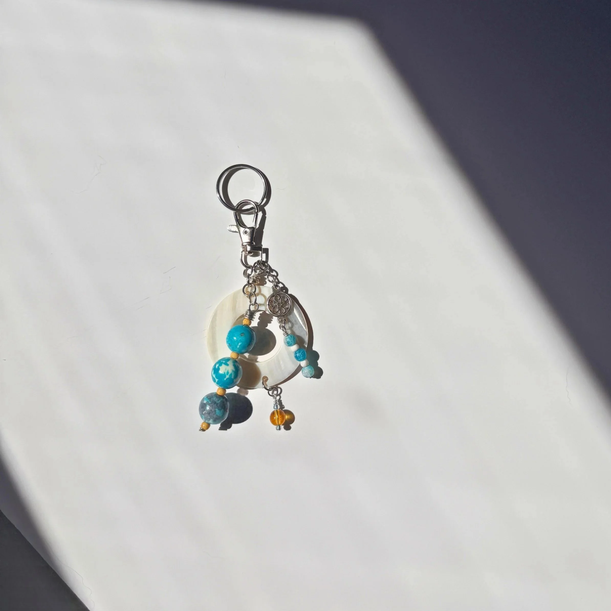 Blue Rain Flower Stone Bag Charm with mother of pearl and metal flower charm on light background