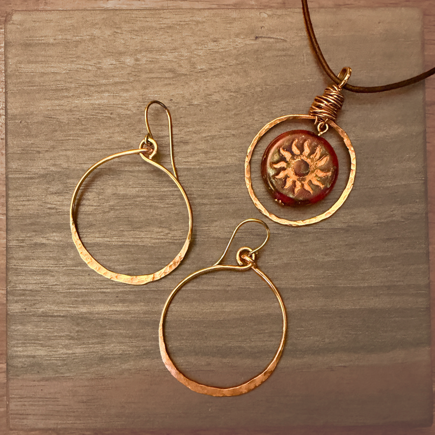 Hammered copper circle earrings shown with copper sol on leather cord necklace on woodon wood