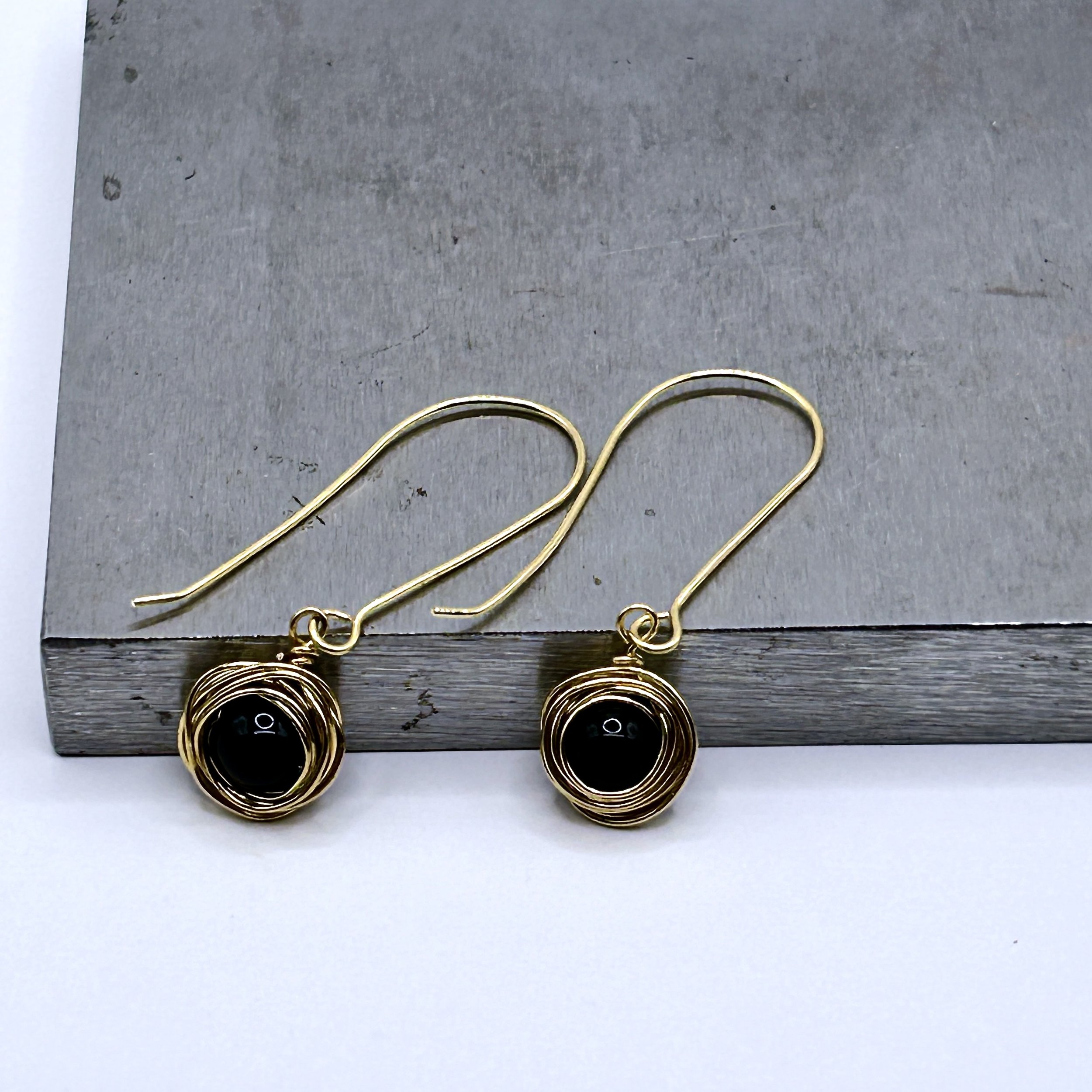 Messy Bun Earring with Black Bead nested in Jeweler's Brass metal and Jeweler's Brass long drop ear wires on metal block