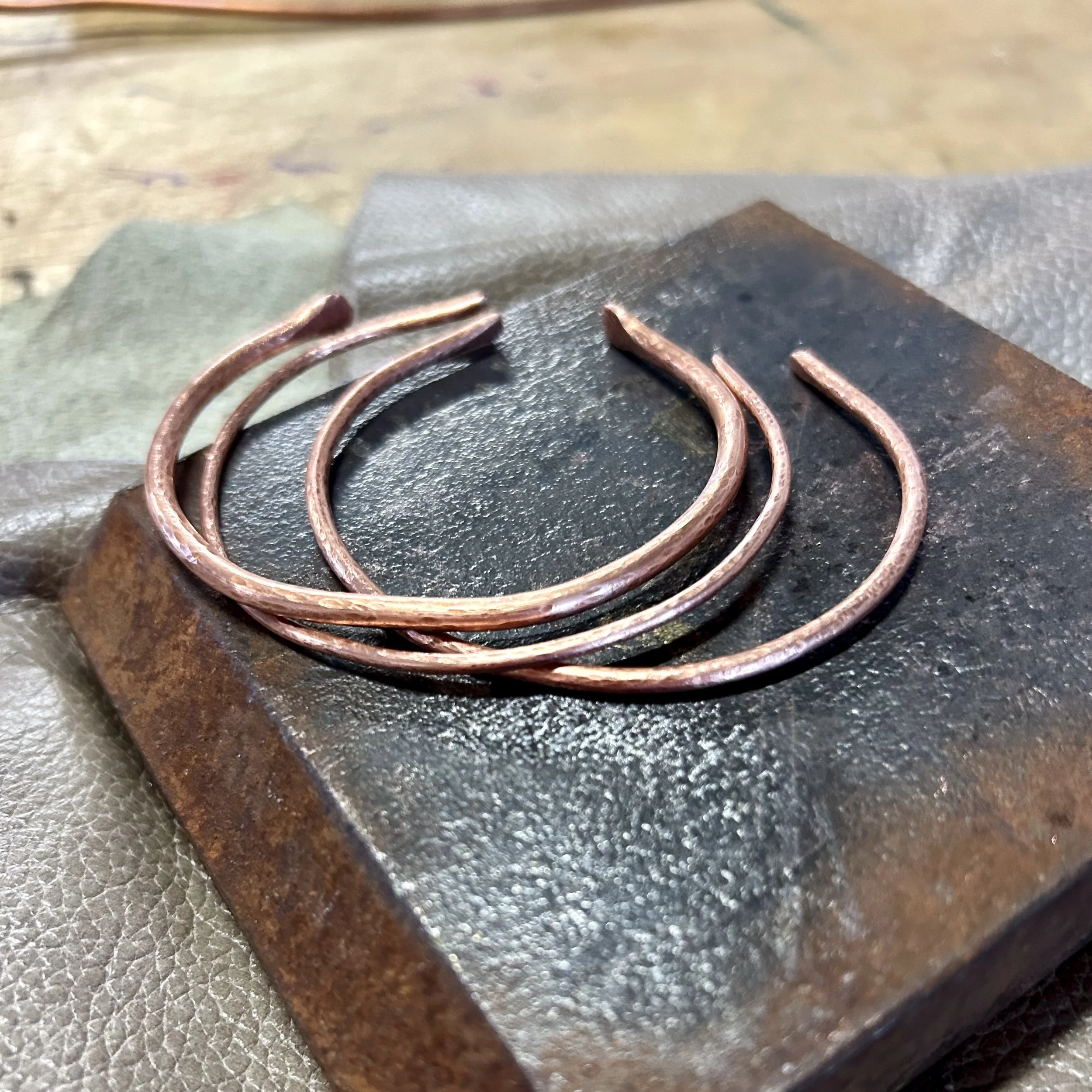 Hand-hammered copper bracelets on workbench