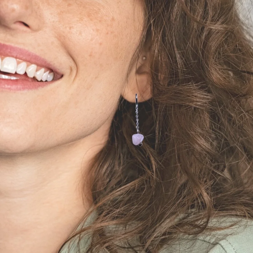 Smiling woman wearing rose quartz earrings dangle from delicate silver plated chains with stainless steel earring hooks on white