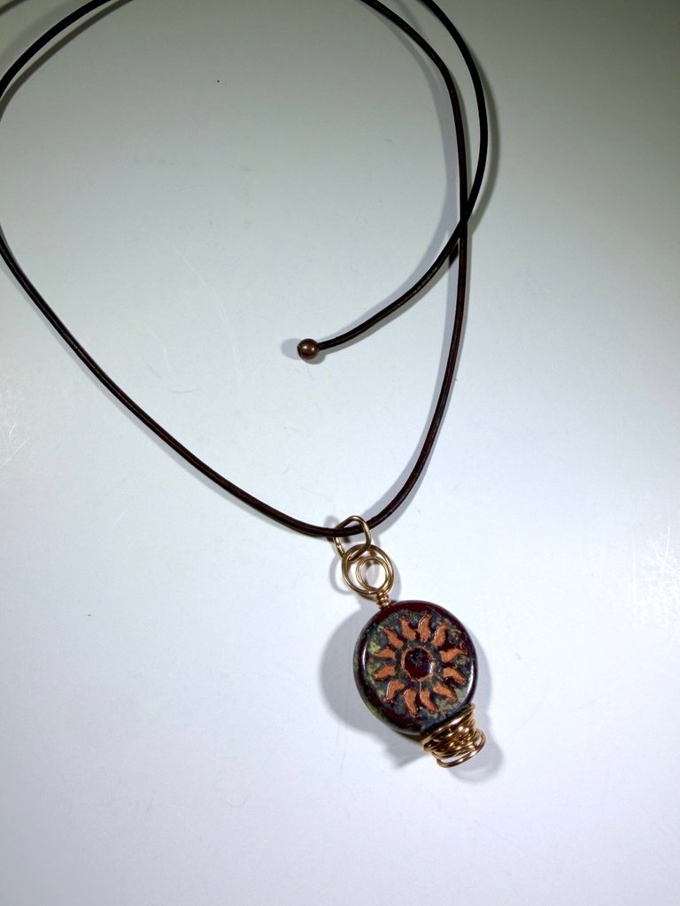 Copper Sol Swirl pendant on leather cord necklace on light background