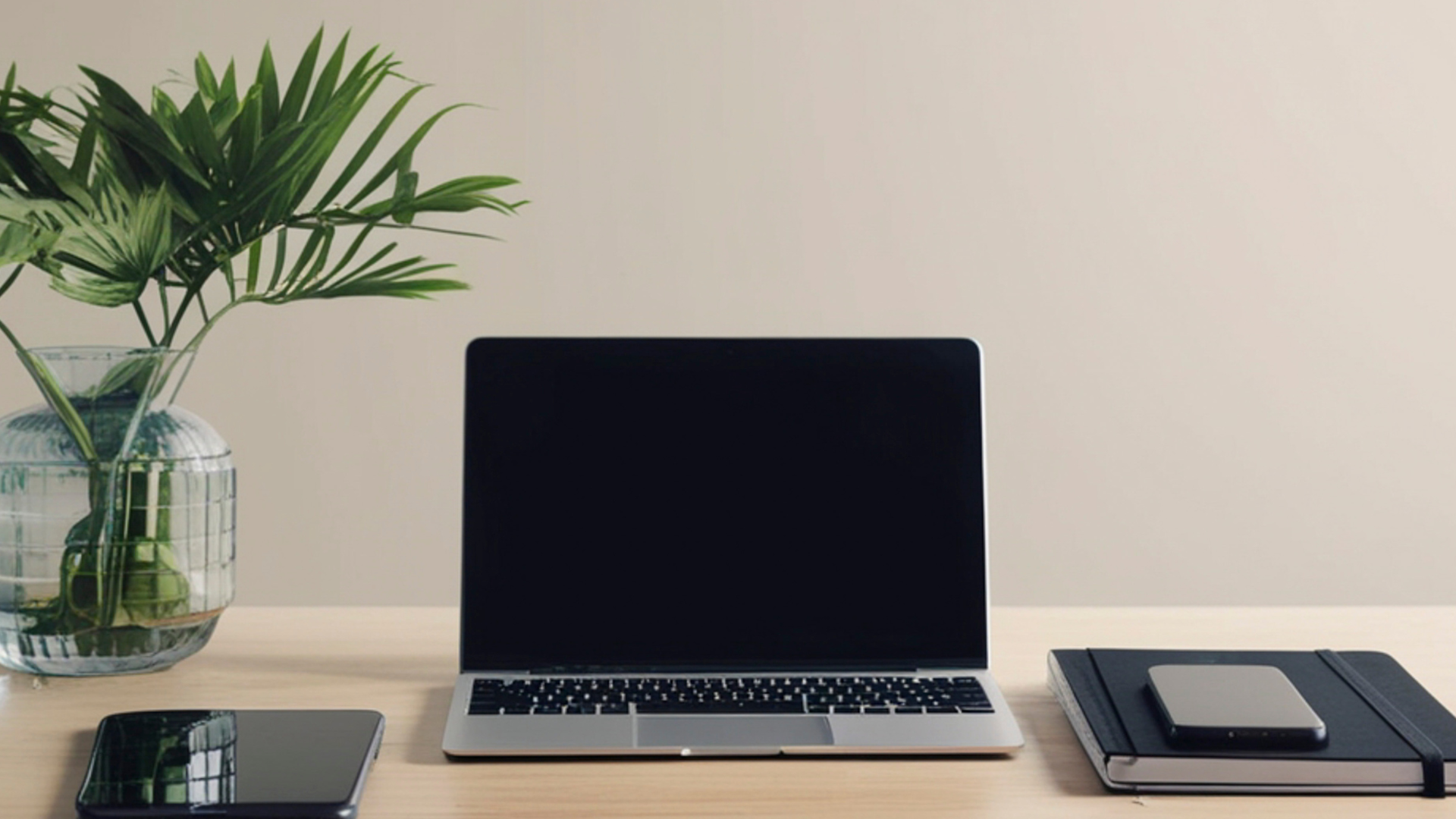 A desk featuring a green plant, a tablet, a laptop, a notebook, and a cell phone.