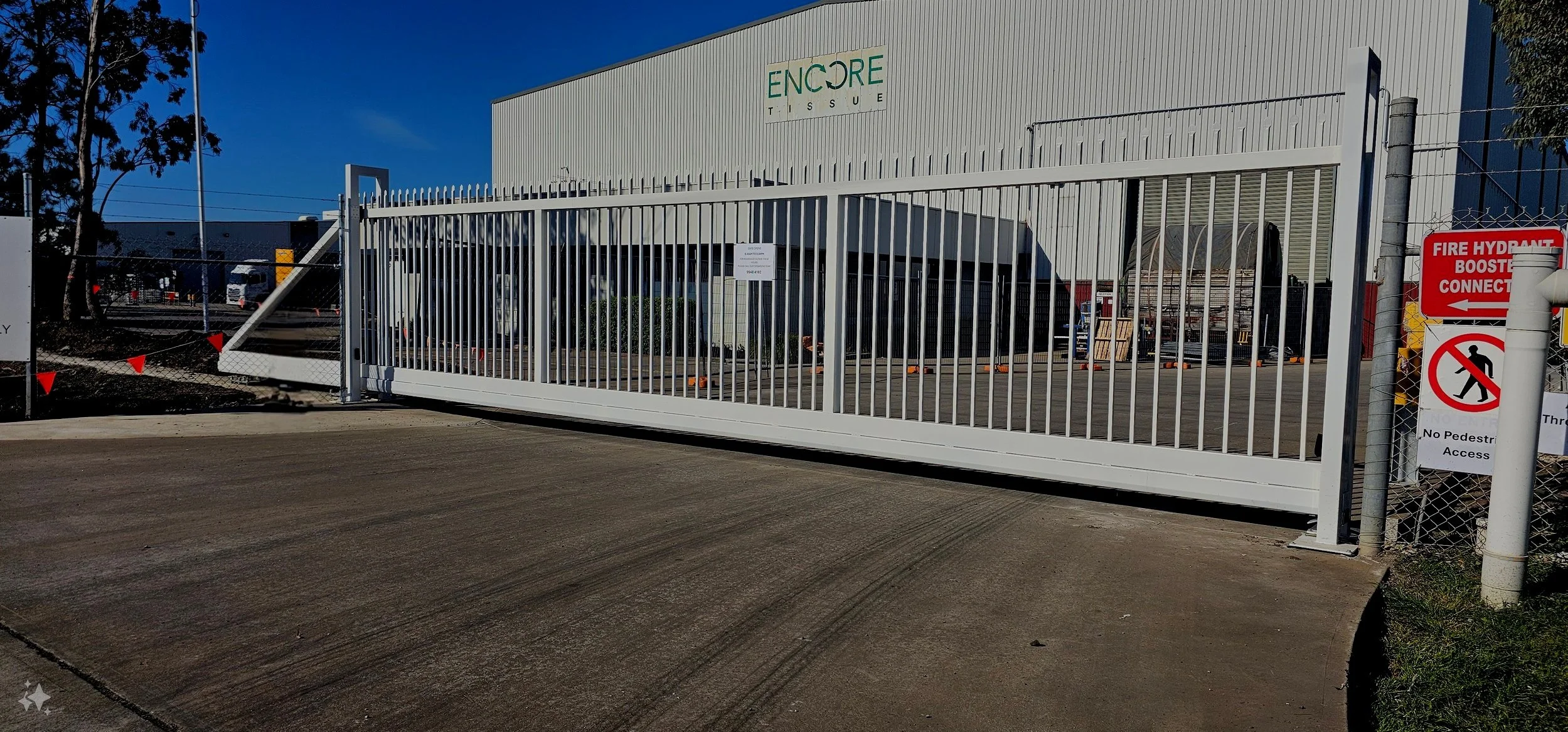 Large industrial building with a white fence and gate, featuring signage for restricted access and a fire hydrant connection. The building has the word 'ENCOR' partially visible.
