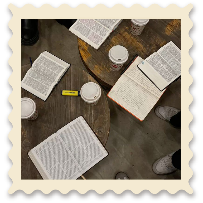 Mesas de madera con libros y cuadernos abiertos, y varias bebidas en vasos con tapa, en un ambiente interior.