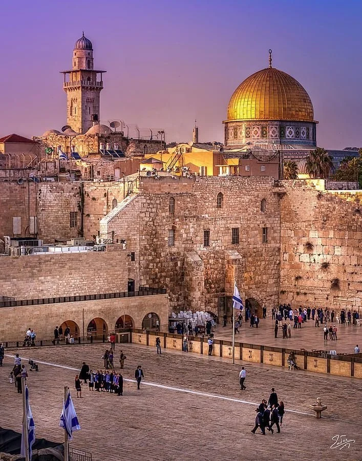 Vista de Jerusalén con el Muro de los Lamentos en primer plano y la Cúpula de la Roca dorada en el fondo, durante el atardecer.