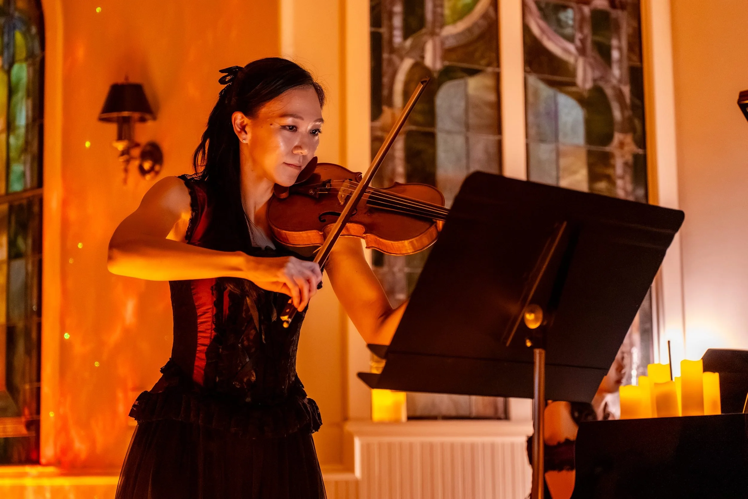 Violinist in a red and black corset dress lit by candles