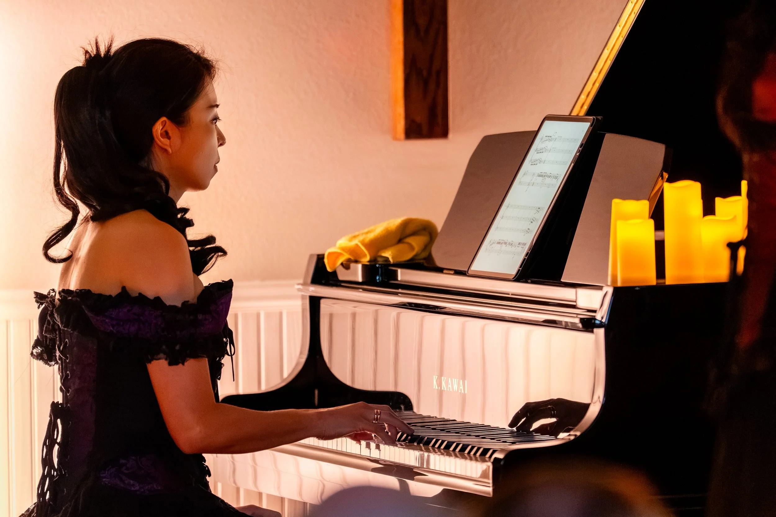 Pianist in a purple off-the-shoulder gown at the Kawai grand, candles on the piano
