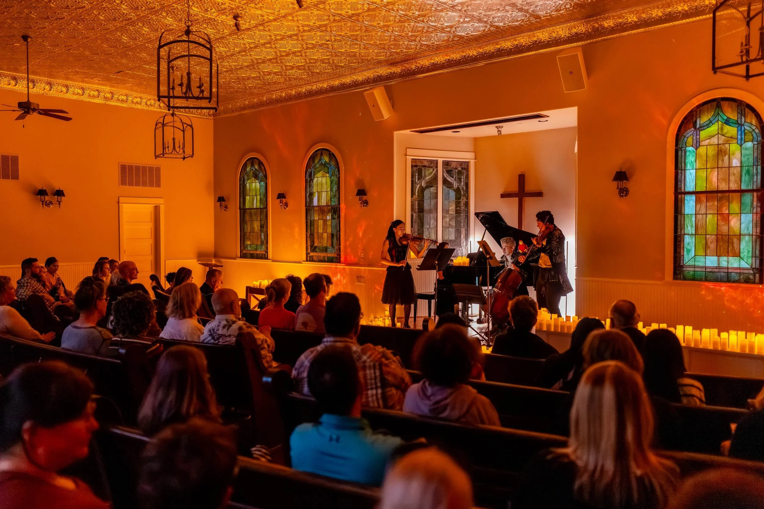 Full chapel under the pressed tin ceiling, musicians performing at the front