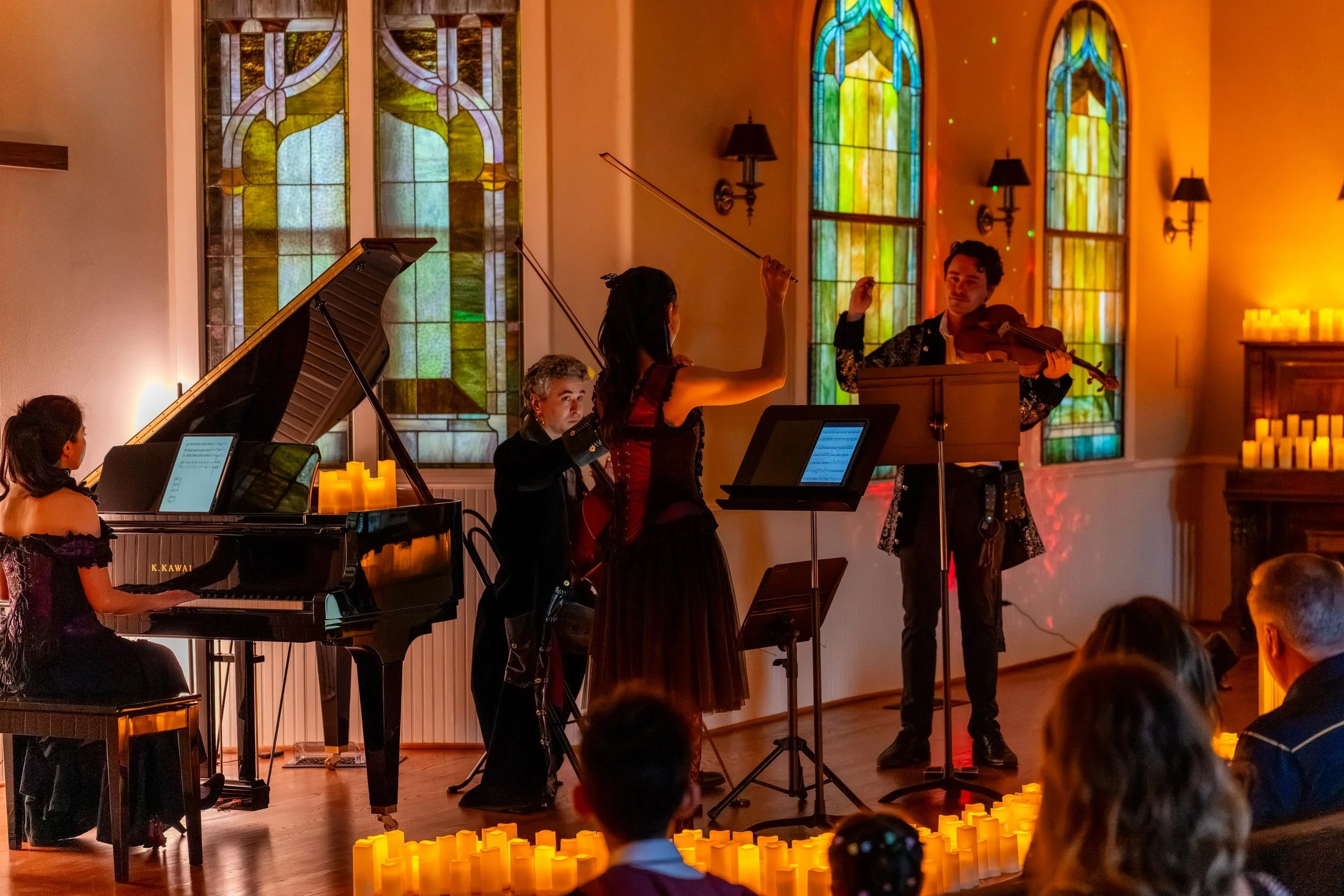 Pianist and string players performing together, candles along the edge of the stage