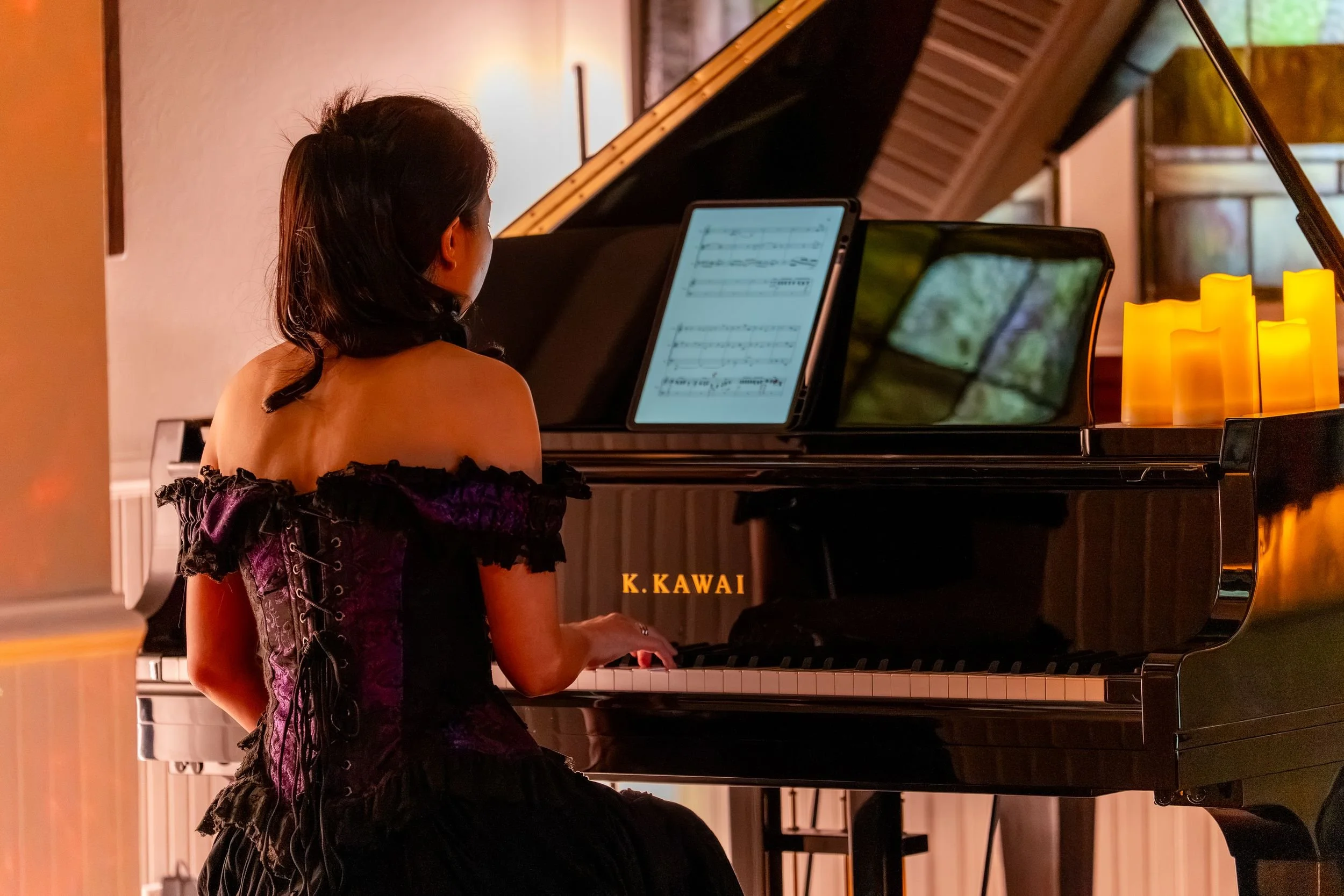 Pianist seen from behind at the Kawai grand piano, candles along the lid