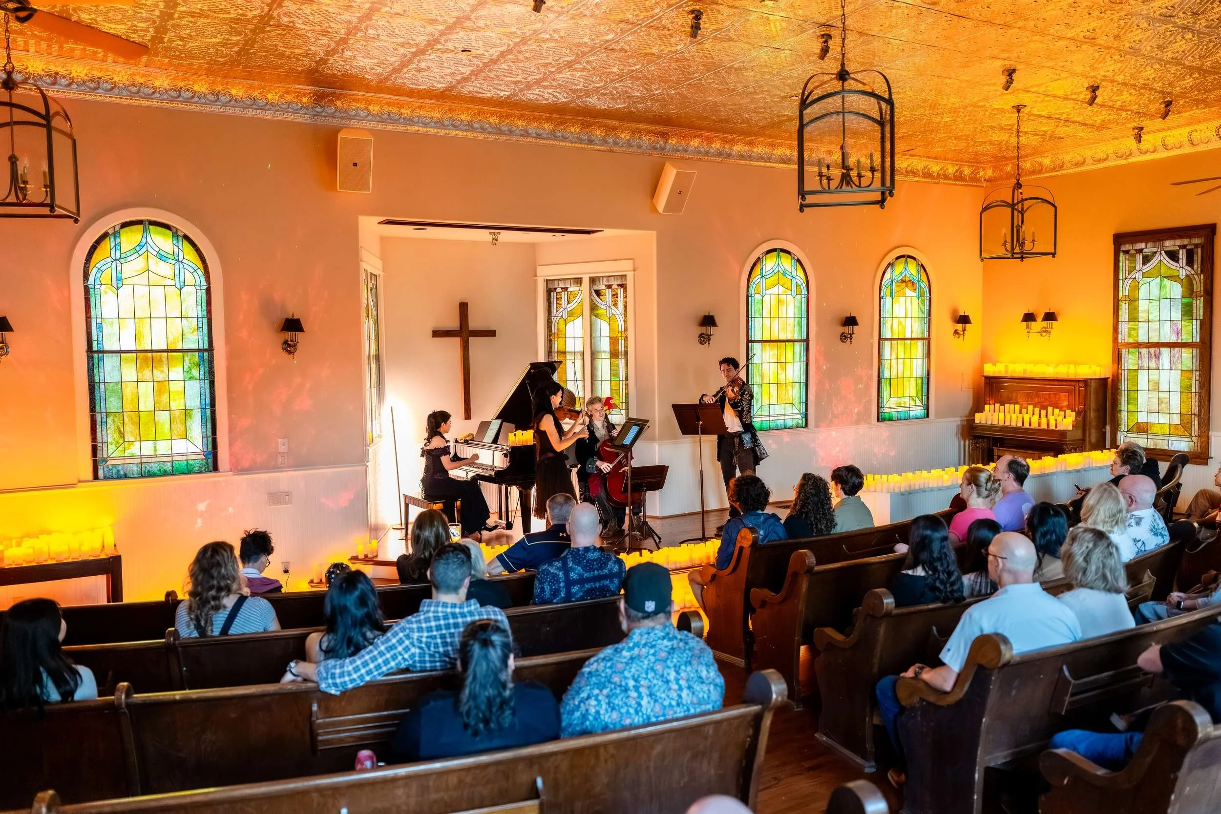Wide view of the candlelit chapel with the audience in the pews and musicians at the front