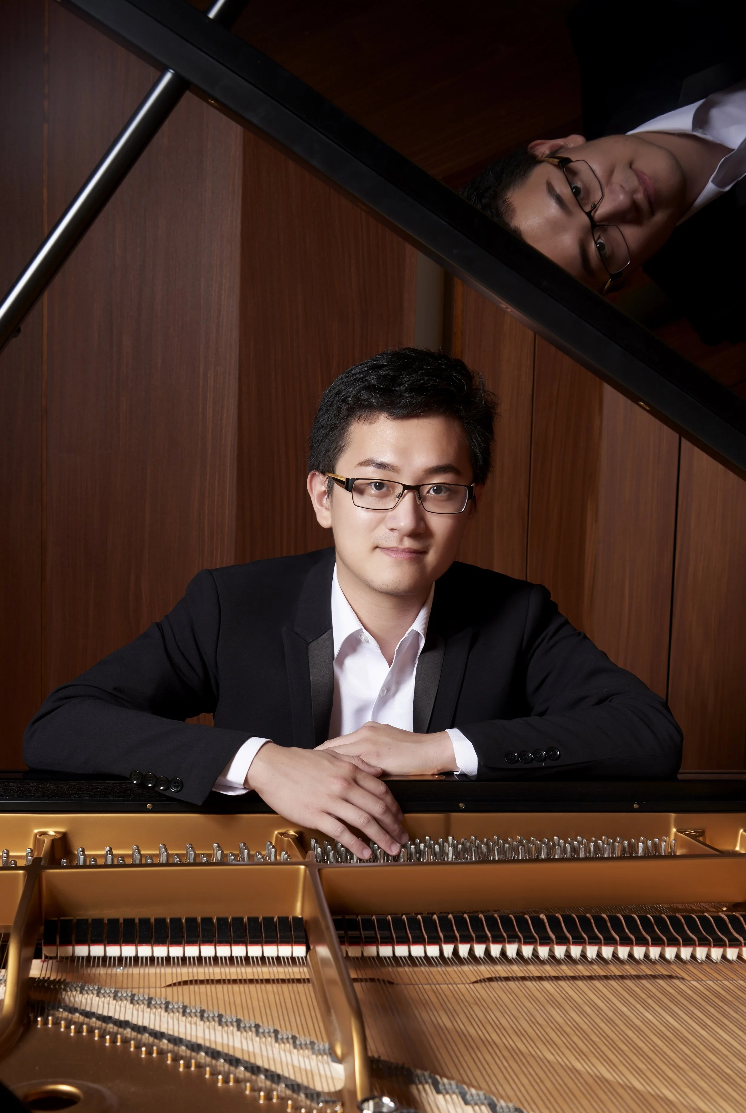Pianist Yi-Chen Feng rests his arms on a piano.