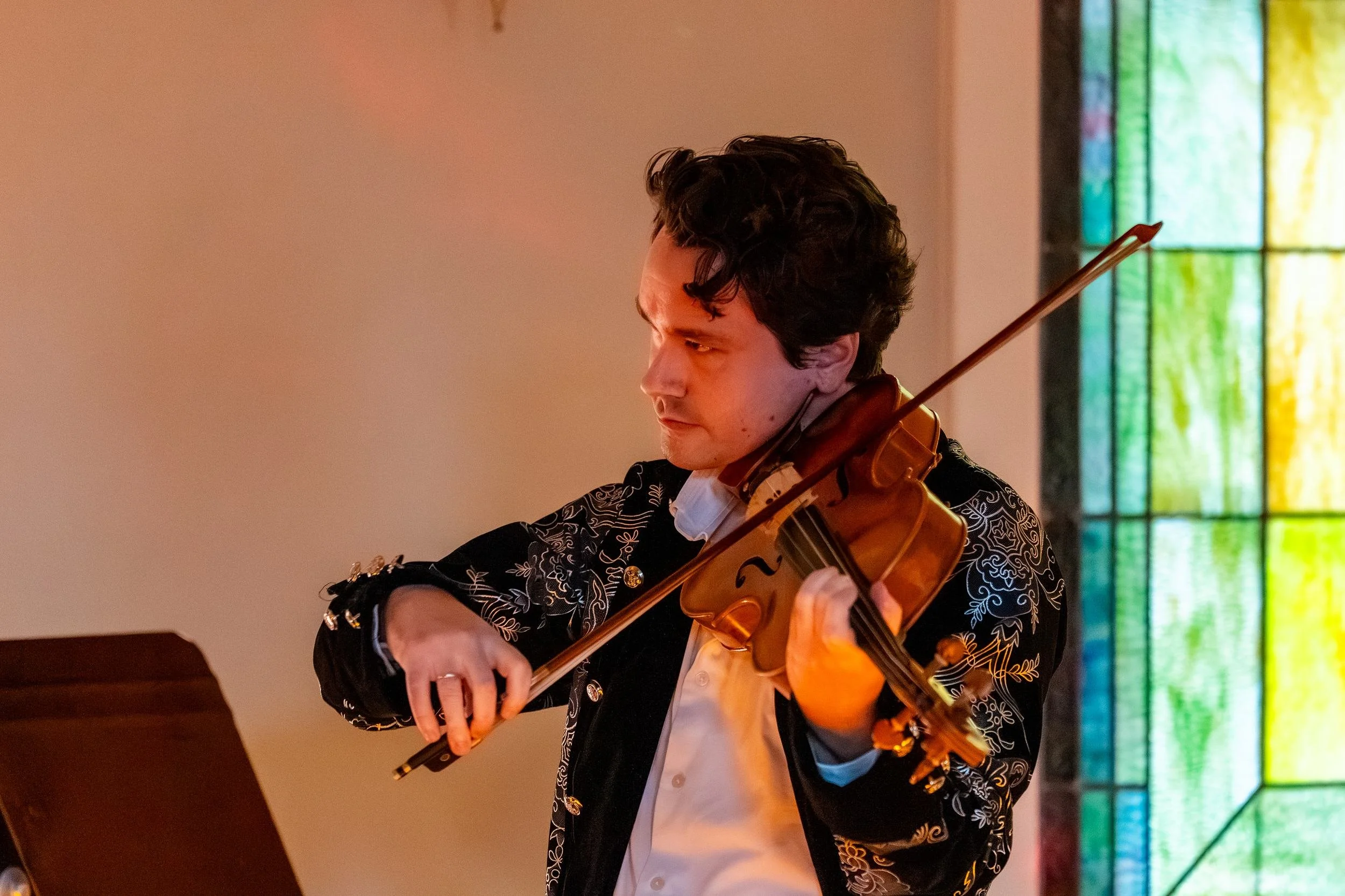 String player in a pirate jacket playing beside a stained glass window