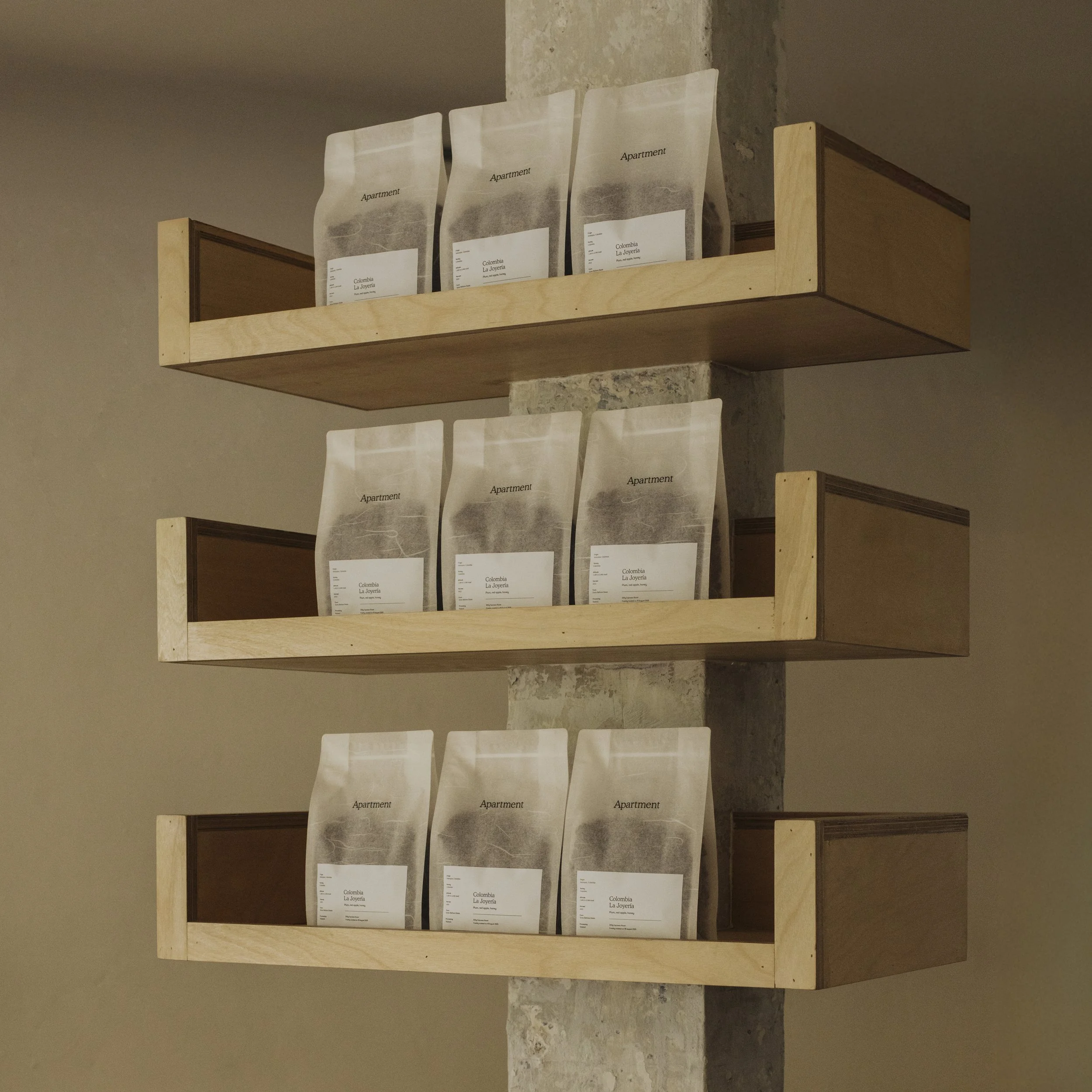 Wooden shelves attached to a concrete wall holding packets labeled 'Apartment' and 'Colombia La Joyería.'