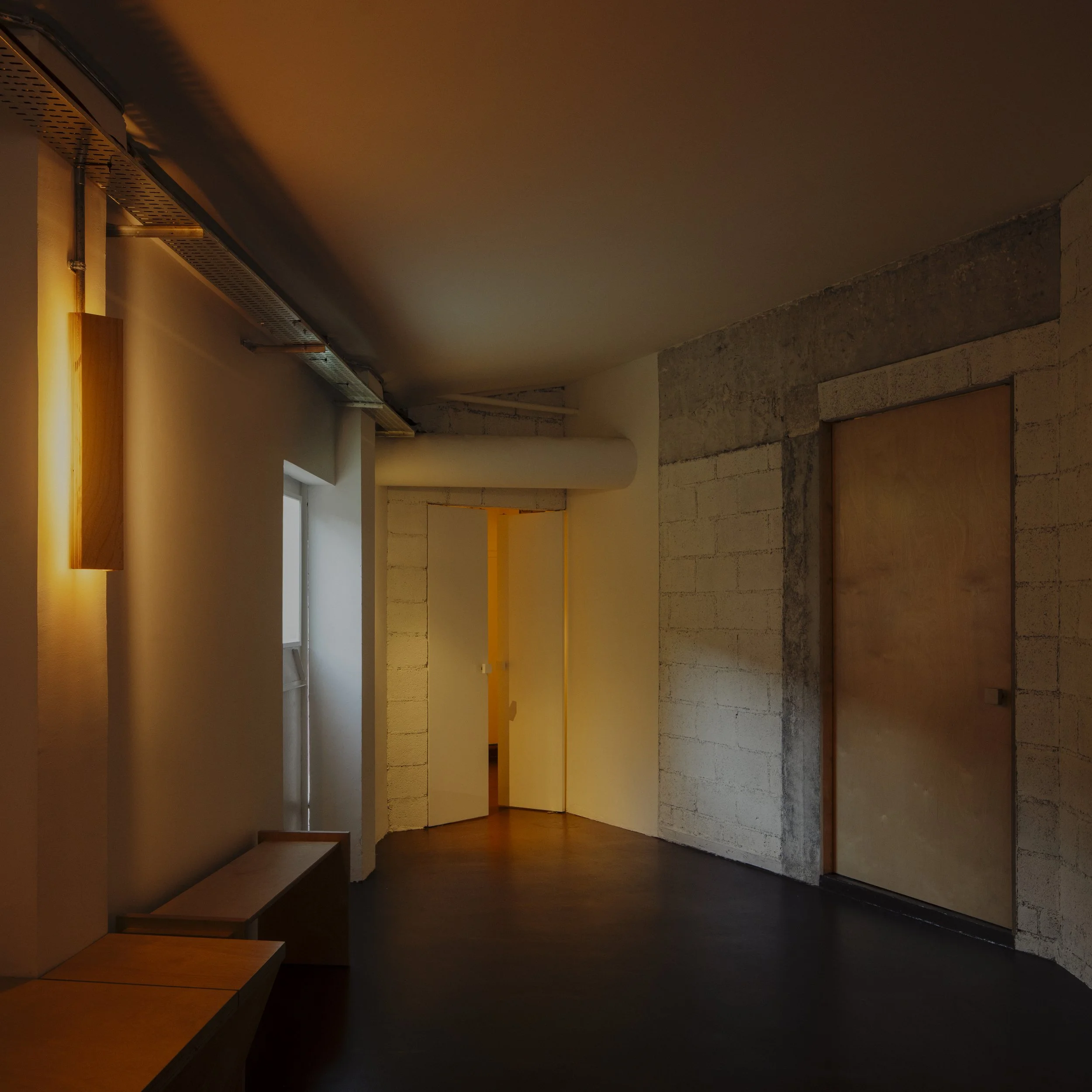 Interior of a modern room with concrete walls, wooden benches, small window, and warm lighting.