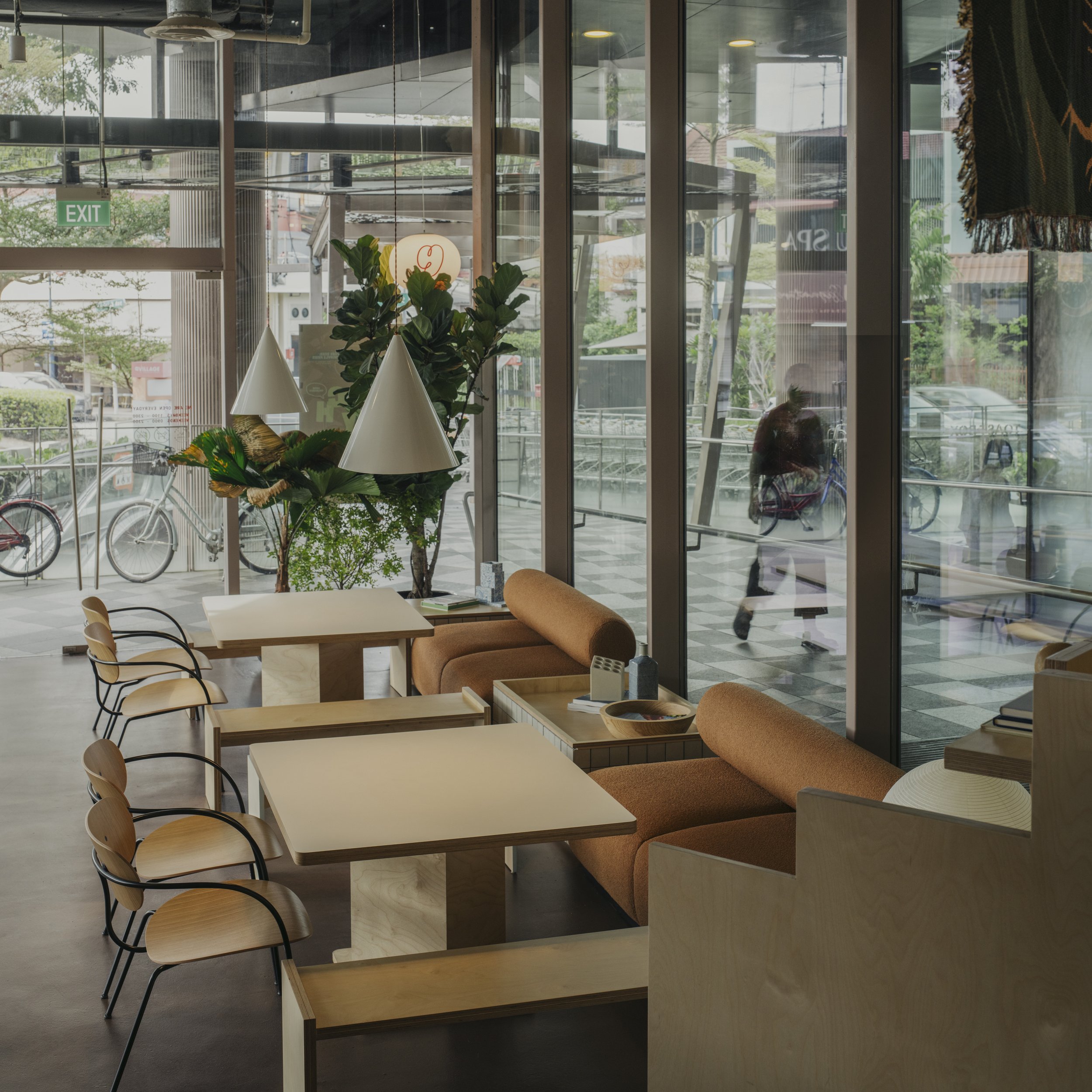 Interior of a modern café with tables, chairs, and cozy seating, large glass windows showing bicycles and street outside.