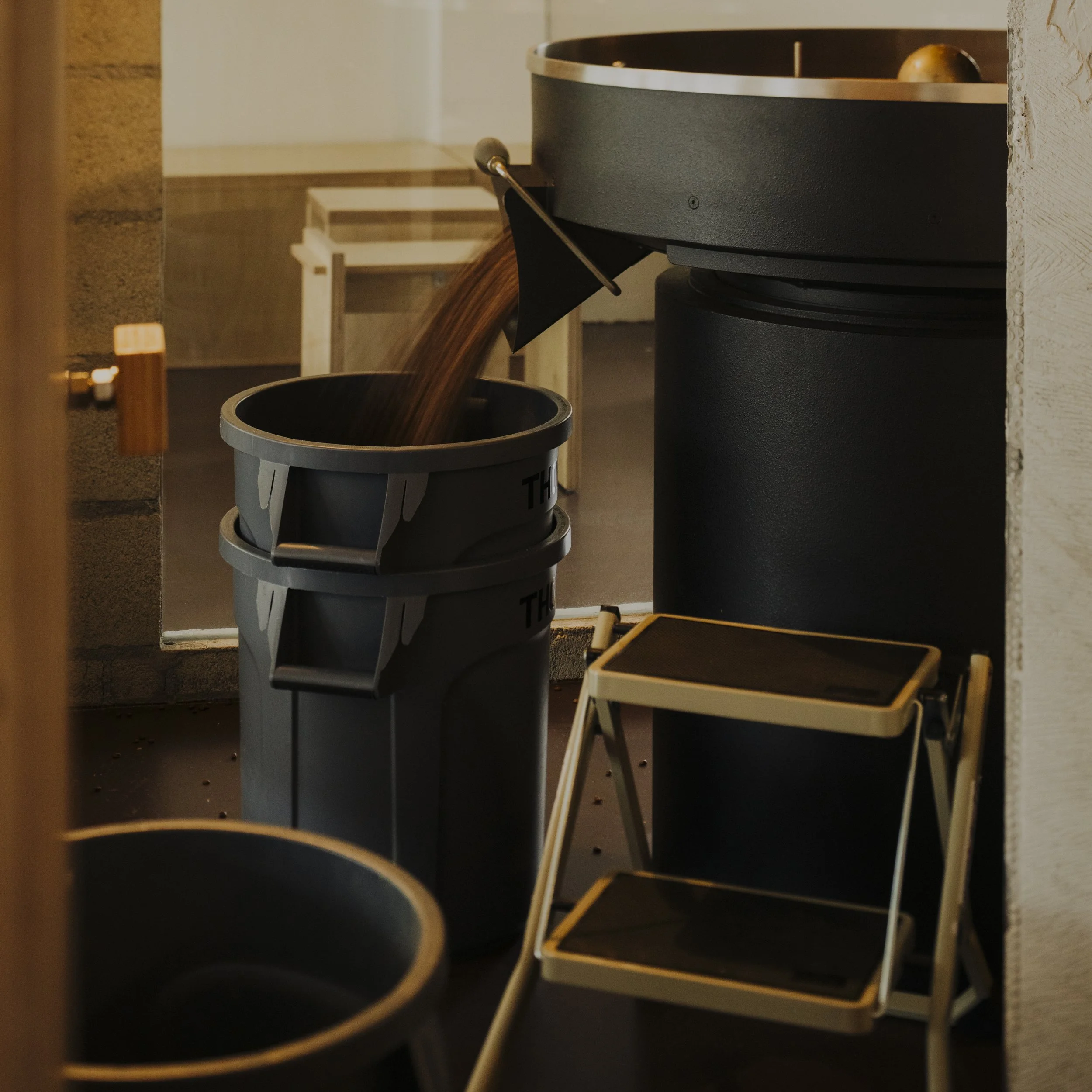 Garbage bin with brown waste being disposed of, a small foldable step stool, and other bins or containers near a doorway.