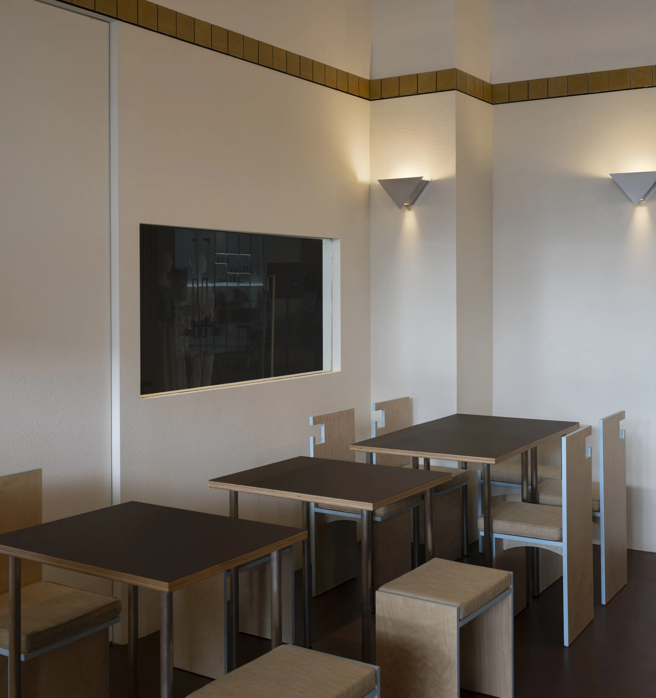 Empty dining area with three tables, six chairs, a window, and wall-mounted lights.