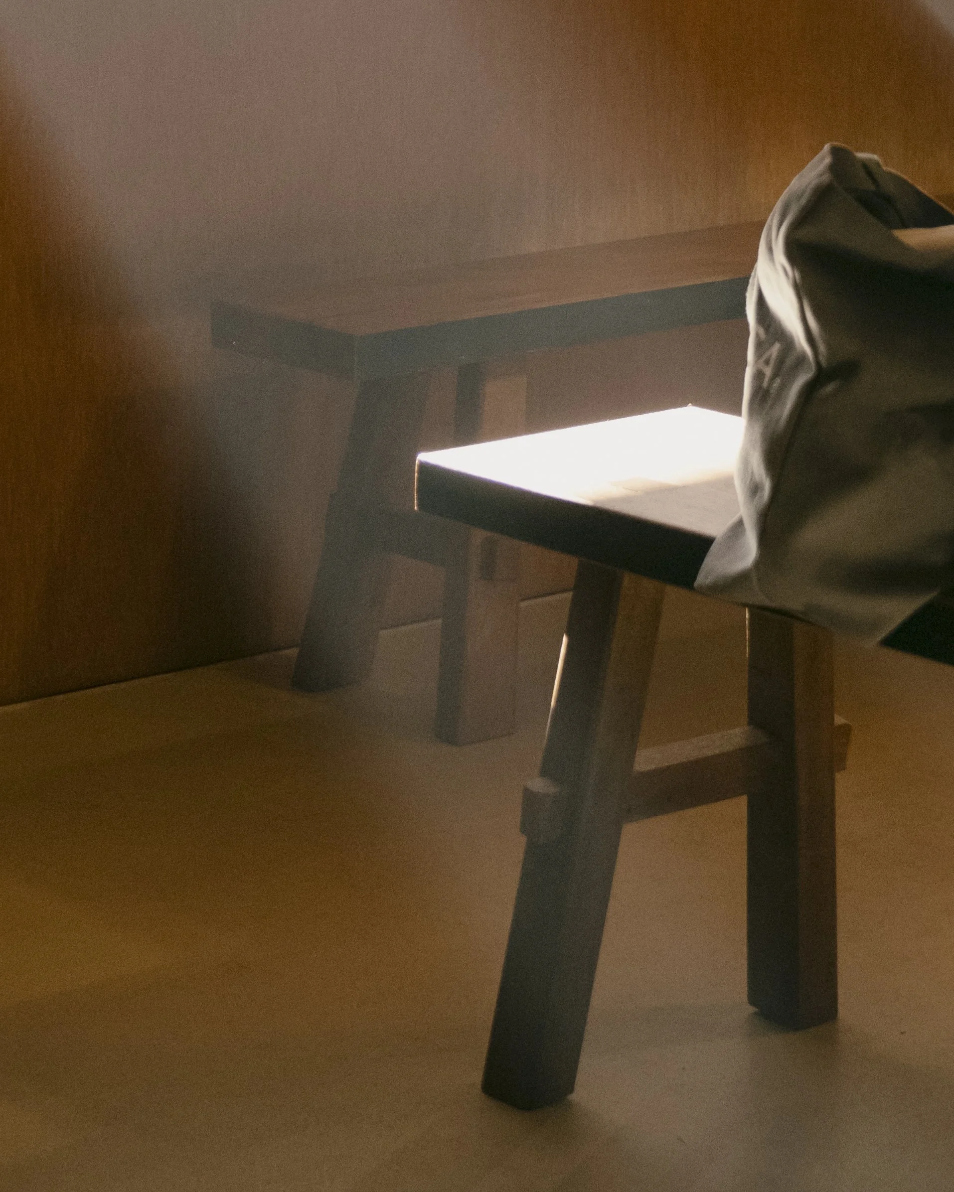 Wooden chair with sunlight streaming on the seat, and a black bag resting on the right armrest.
