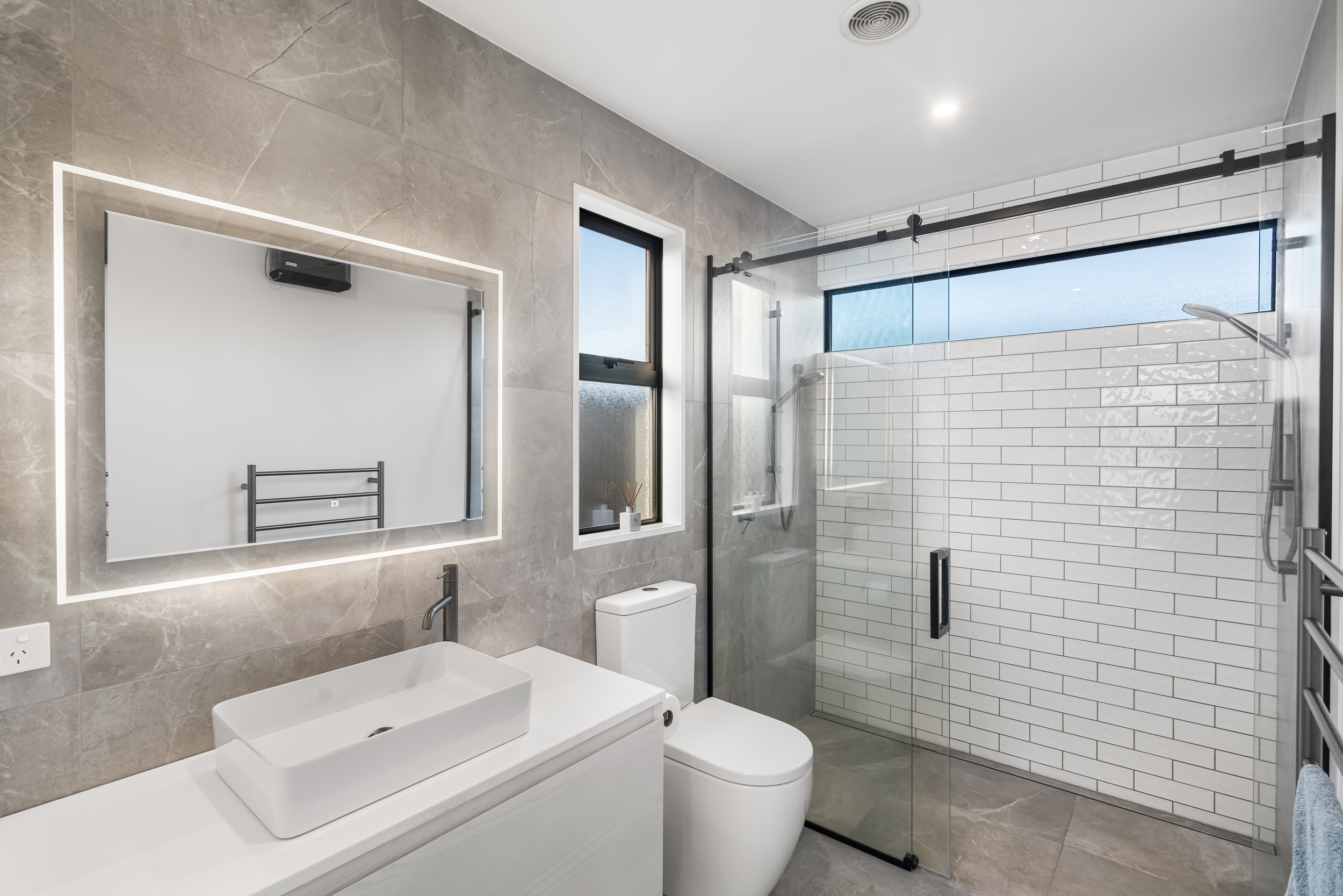 Modern tiled bathroom with large walk in shower with greens tapware and top mounted sink unit.