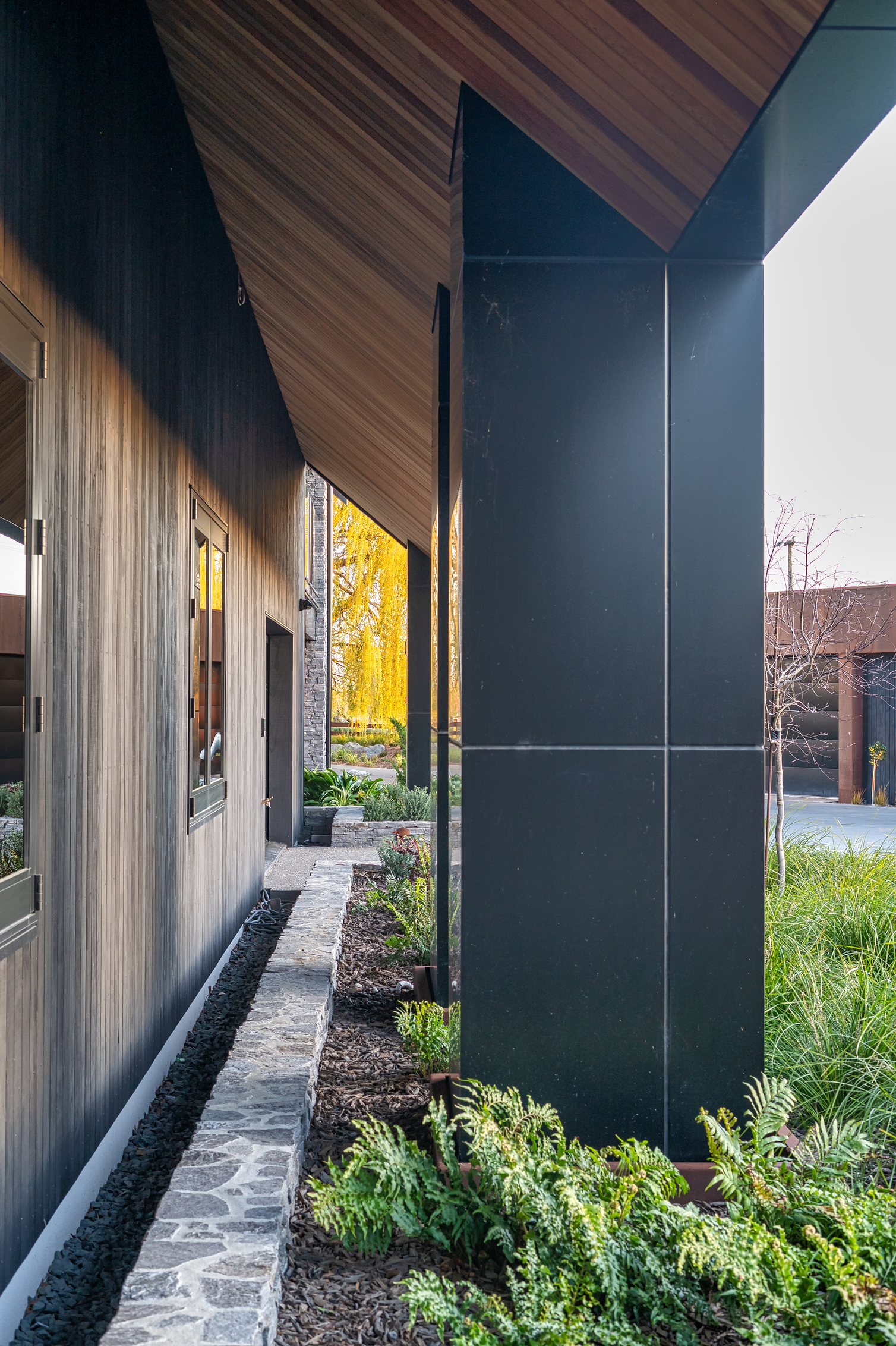 Architectural home entrance with angled cedar roofline and landscaped schist stone garden edging, built by Senna Developments in Christchurch and Canterbury.