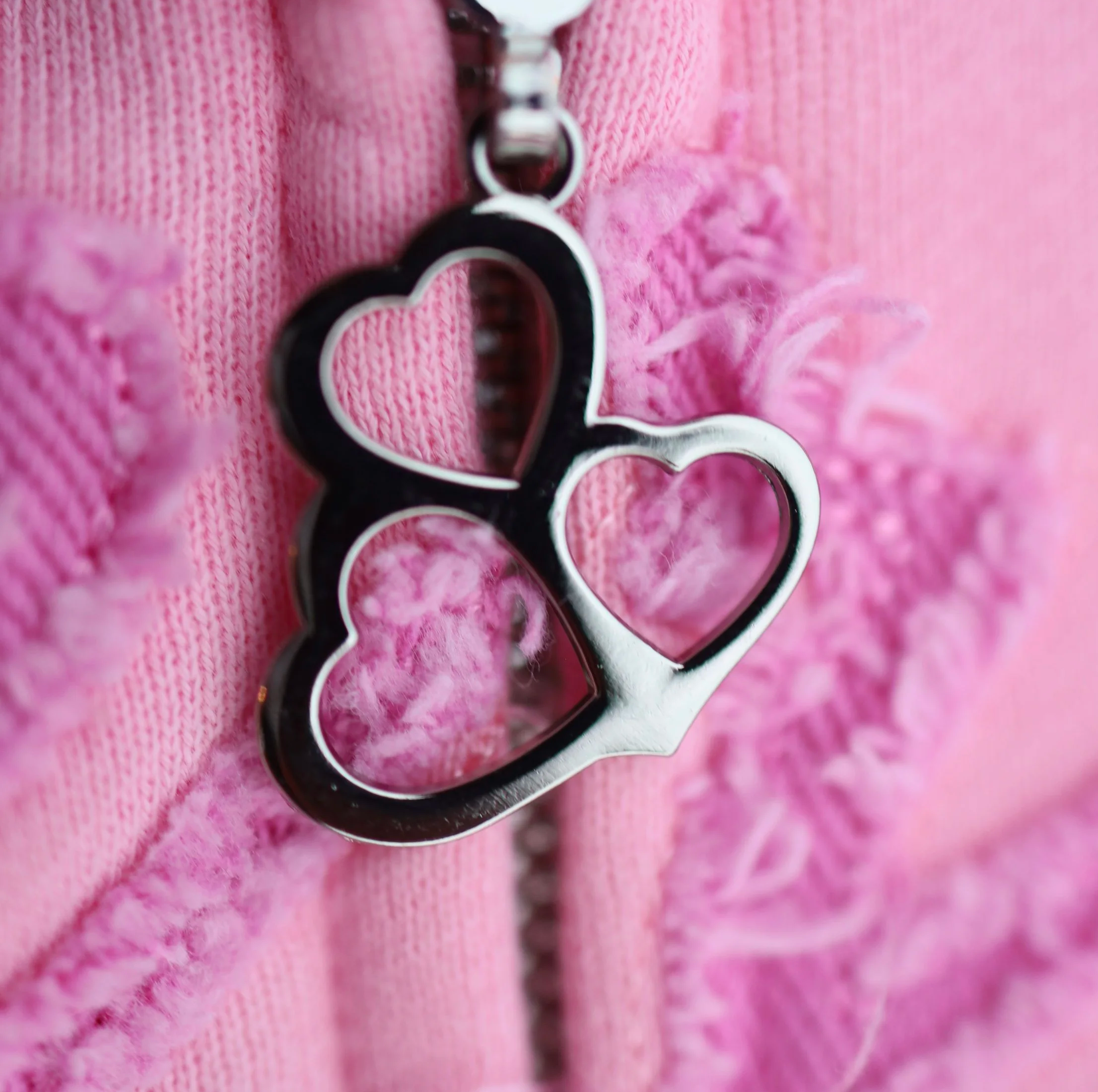 Close-up of a necklace with three connected heart-shaped pendants, set against a pink fleece jacket.