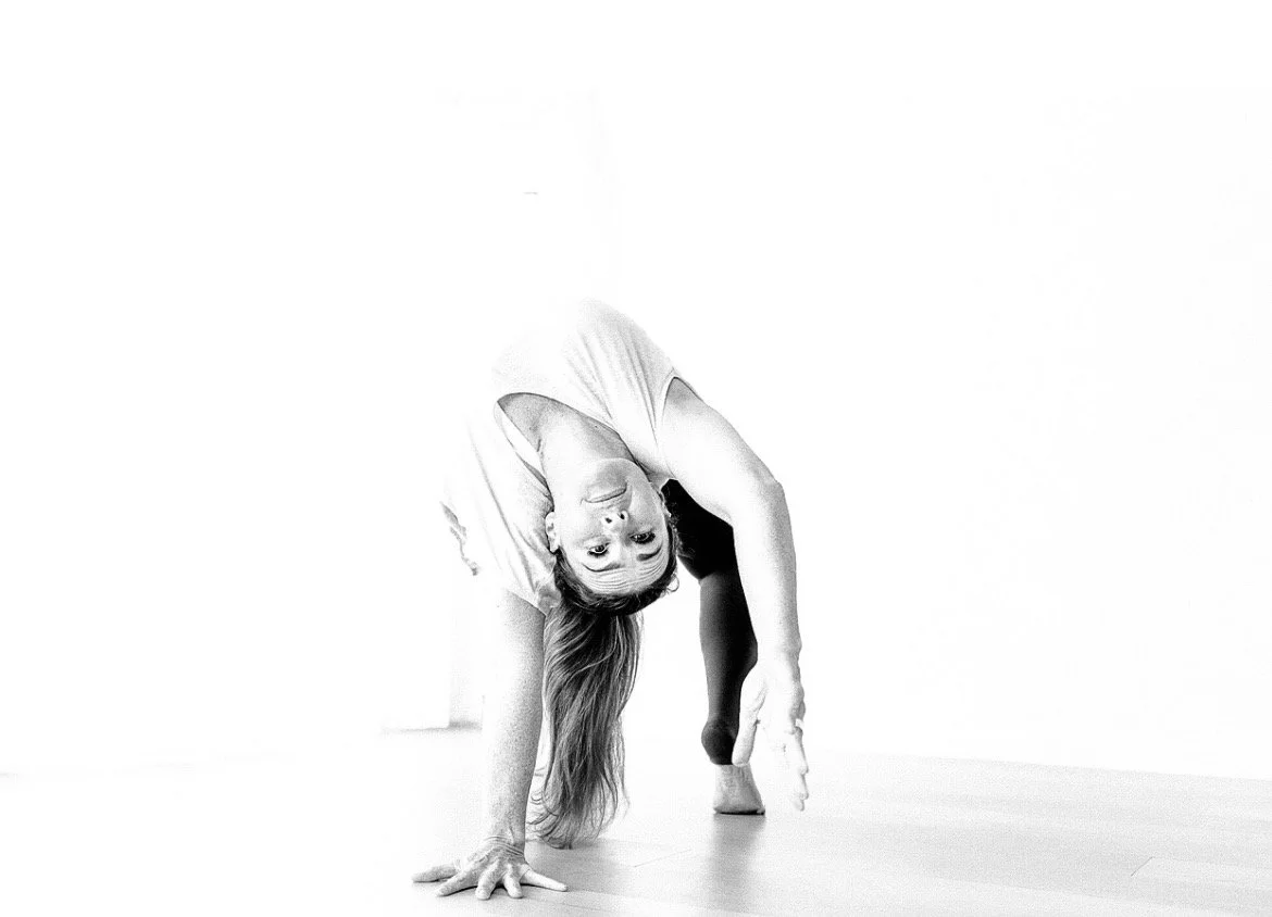 A woman practicing yoga, performing a one-handed backbend pose in a bright, minimalist space.