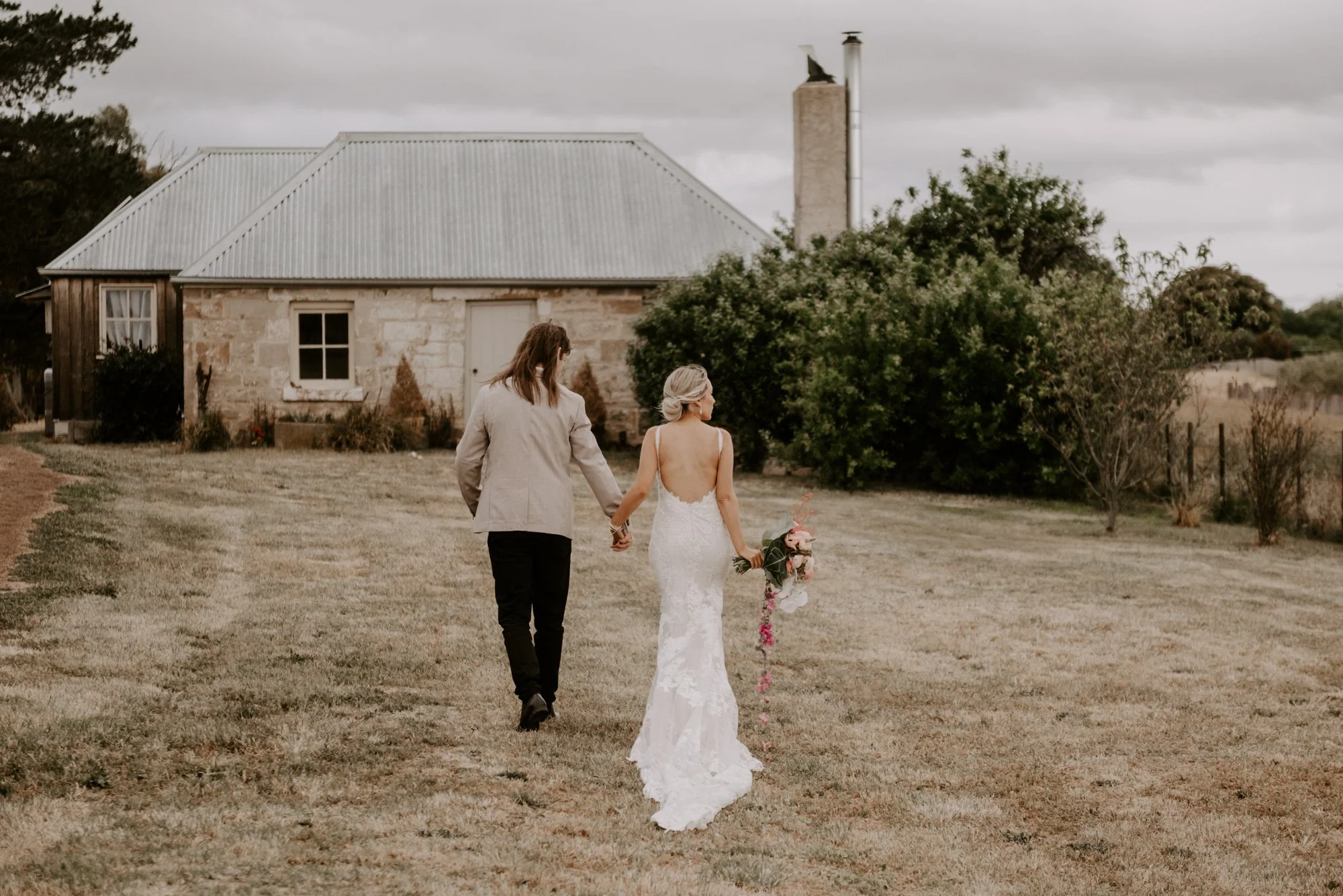 Bride and groom strolling in front of a charming stone cottage during their Tasmania elopement