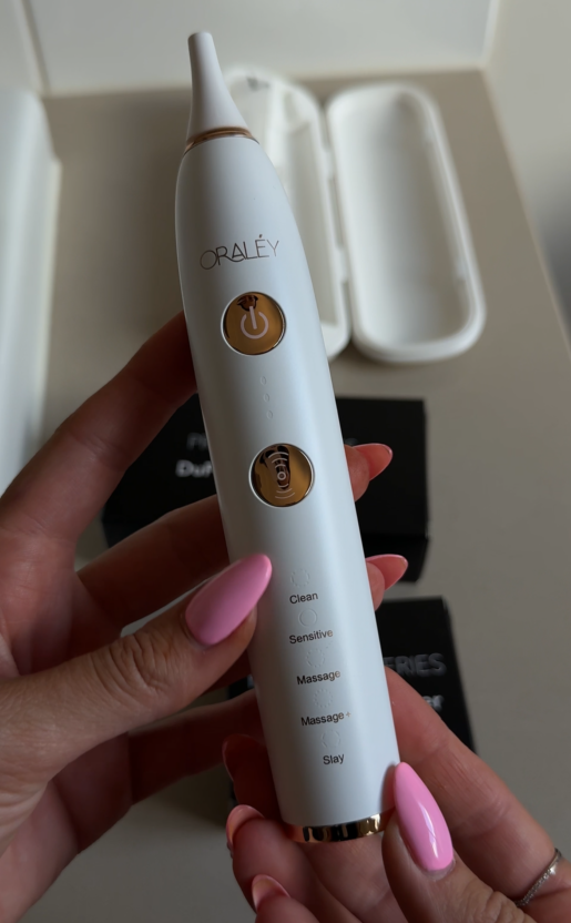 A person's hand holding an Oral-B electric toothbrush with charger features and settings, with an open white case in the background.