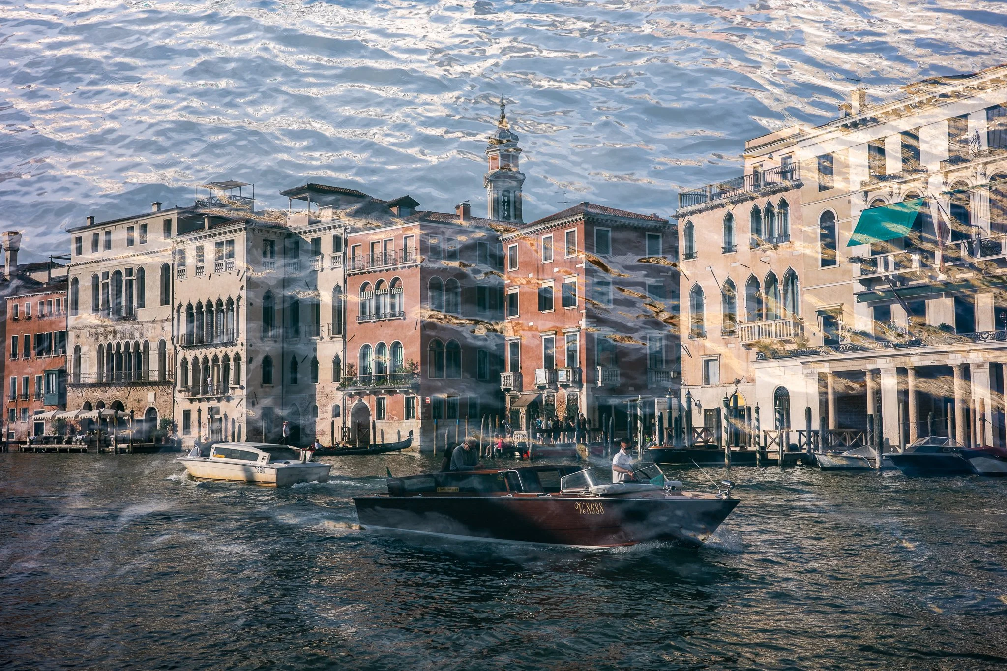 A double exposure of palazzi along the Grand Canal with water taxis passing in front, overlaid with rippled water that fills the upper half of the frame and washes across the buildings as a textured pattern.