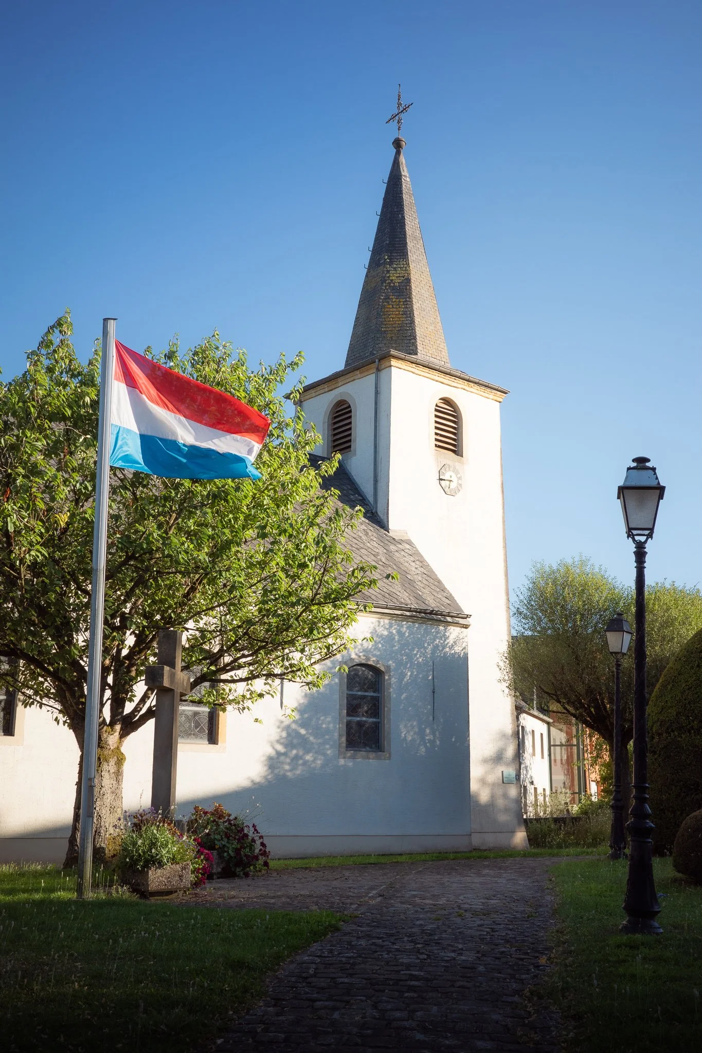 Small church with steeple and Luxembourg flag in front, photographed with the Ricoh GR IIIx.
