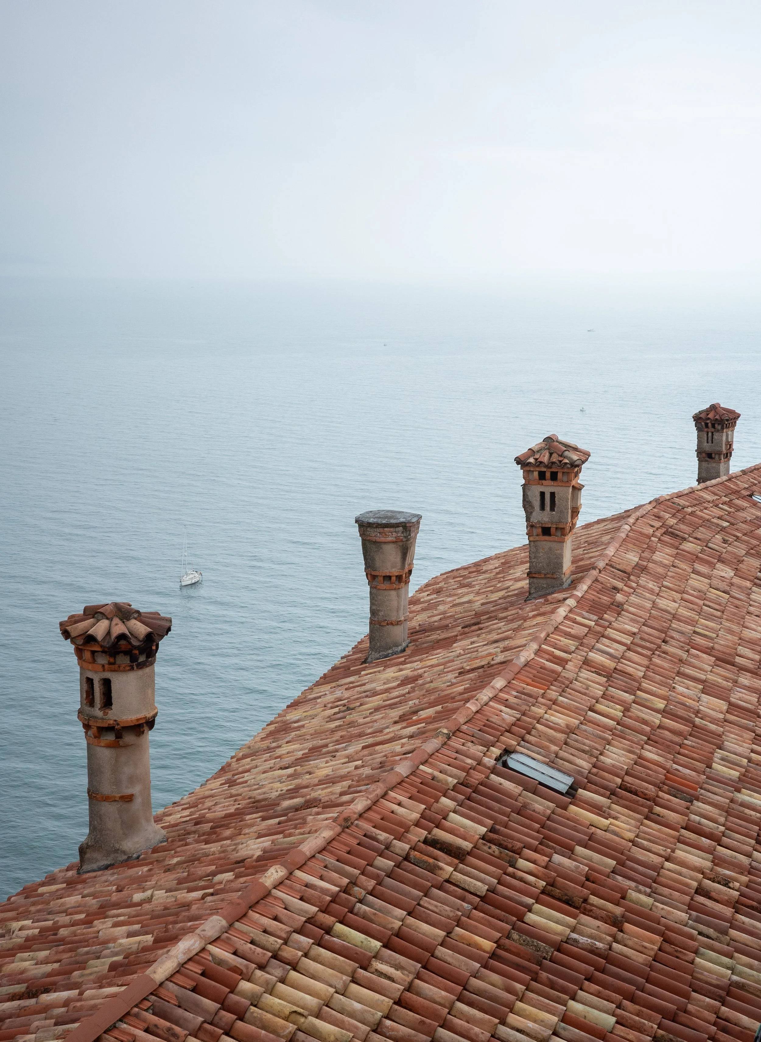 Terracotta rooftop of Duino Castle with several old chimneys overlooking the calm Adriatic Sea on a misty day