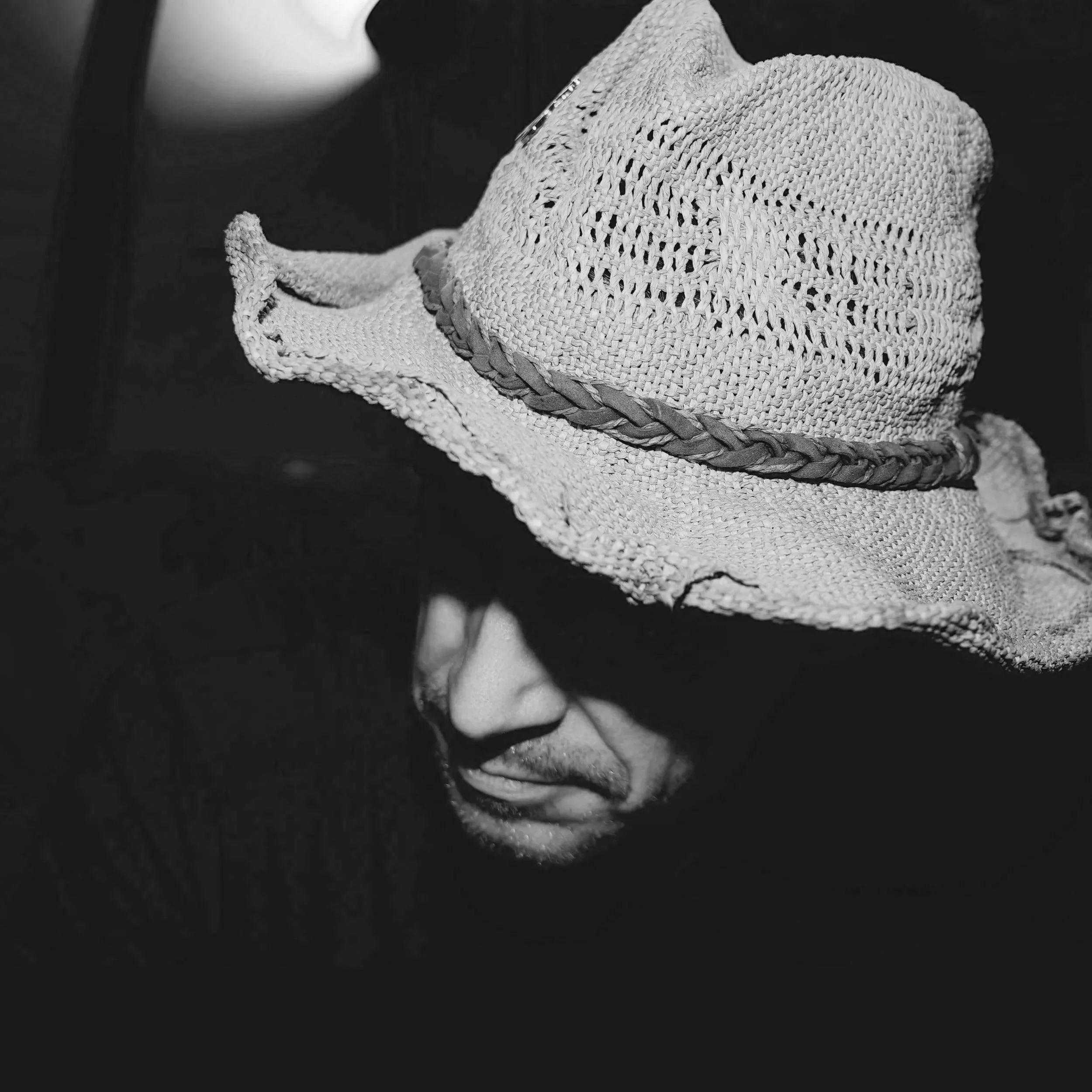Person wearing a wide-brimmed woven straw hat with a braided band, partially visible face, in black and white.