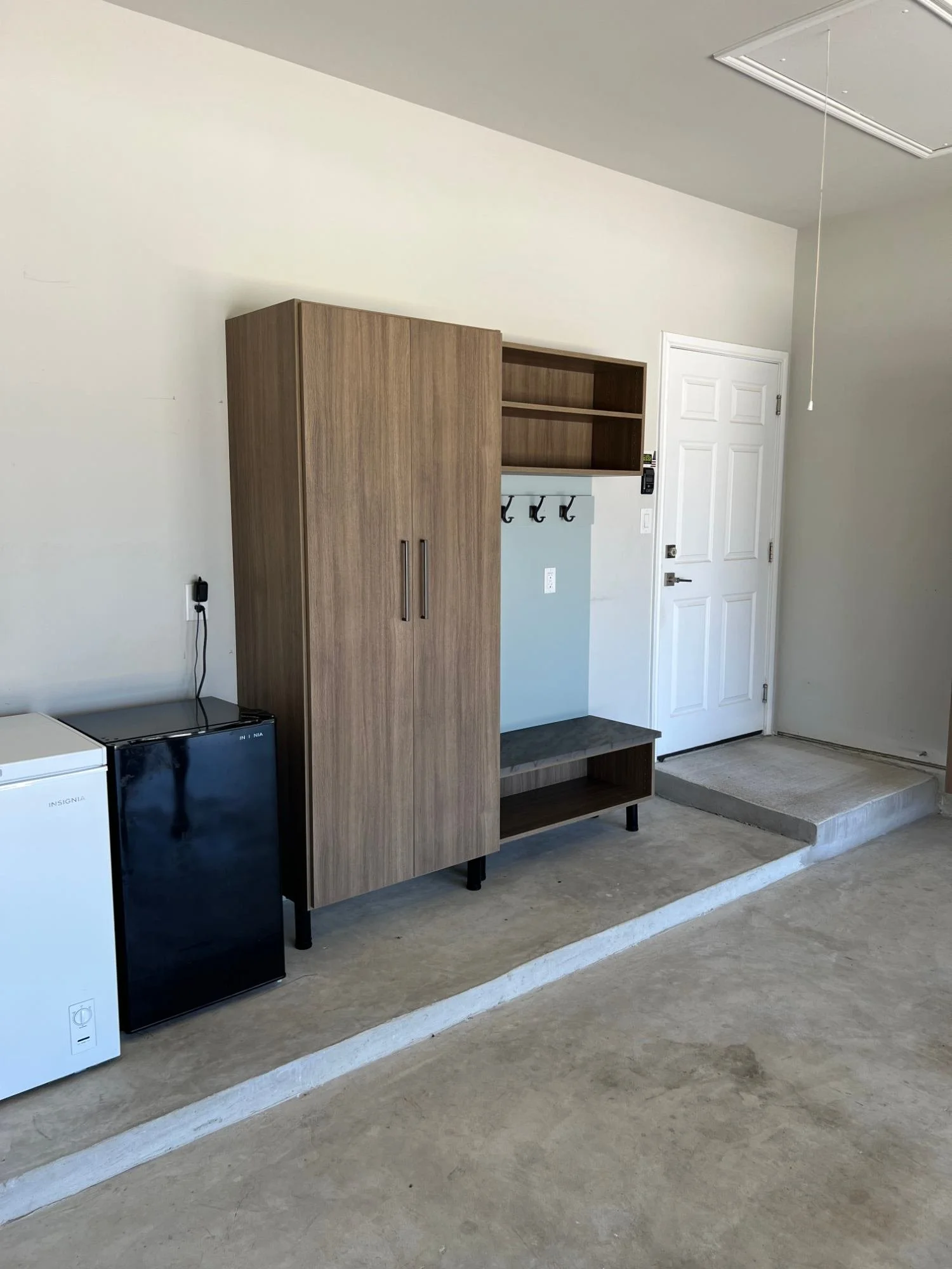 Garage mudroom drop zone with a tall cabinet, coat hooks, open shelves, and a bench beside the door into the house