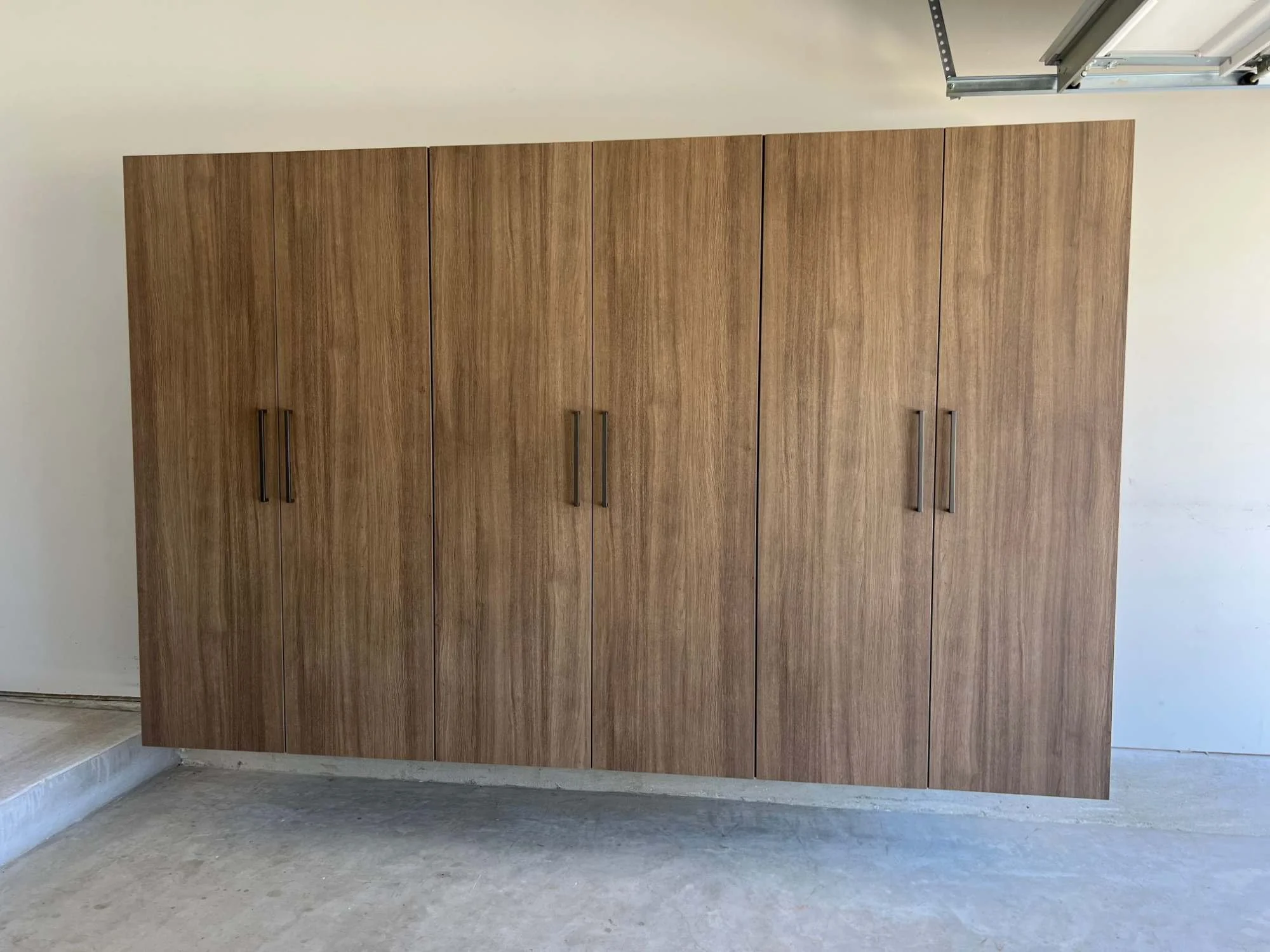 Six-door floating garage cabinets in a warm wood-grain finish with bronze pulls, mounted above the garage floor