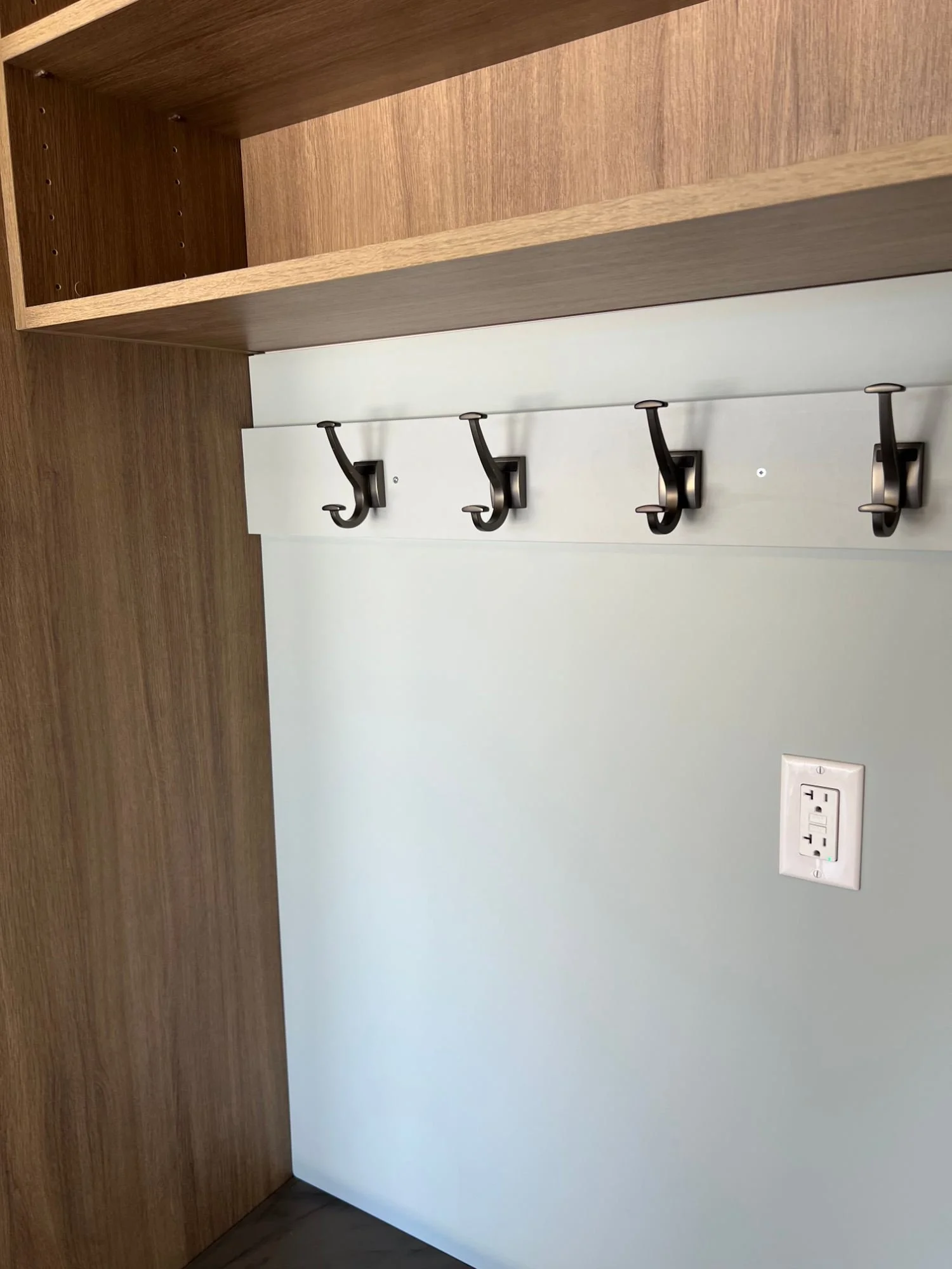 Bronze coat hooks on a soft gray backer panel beneath an open wood-grain shelf
